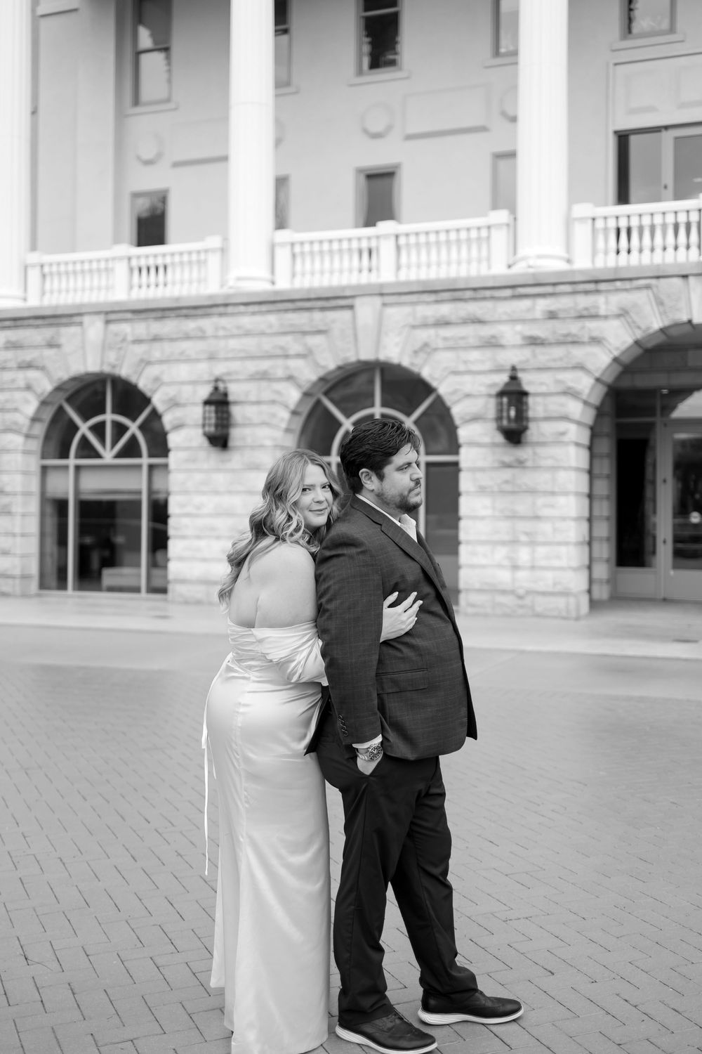 A series of black and white photos showing a romantic moment between two people outside a grand stone building.