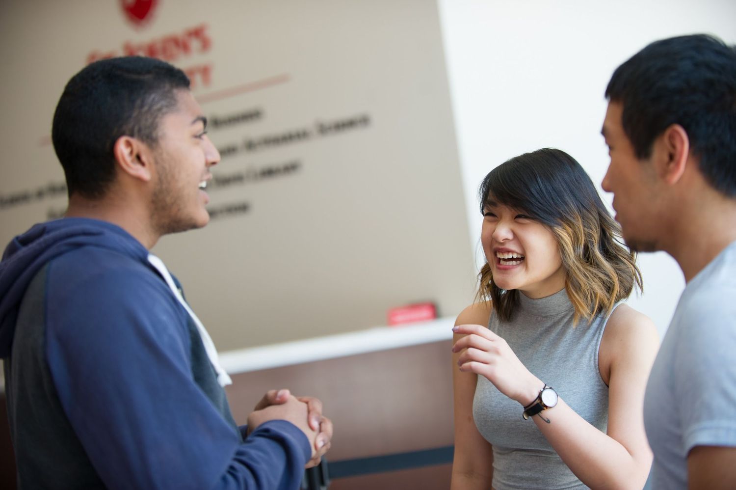 Students engage in lively conversation while standing in a modern indoor hallway or office space.