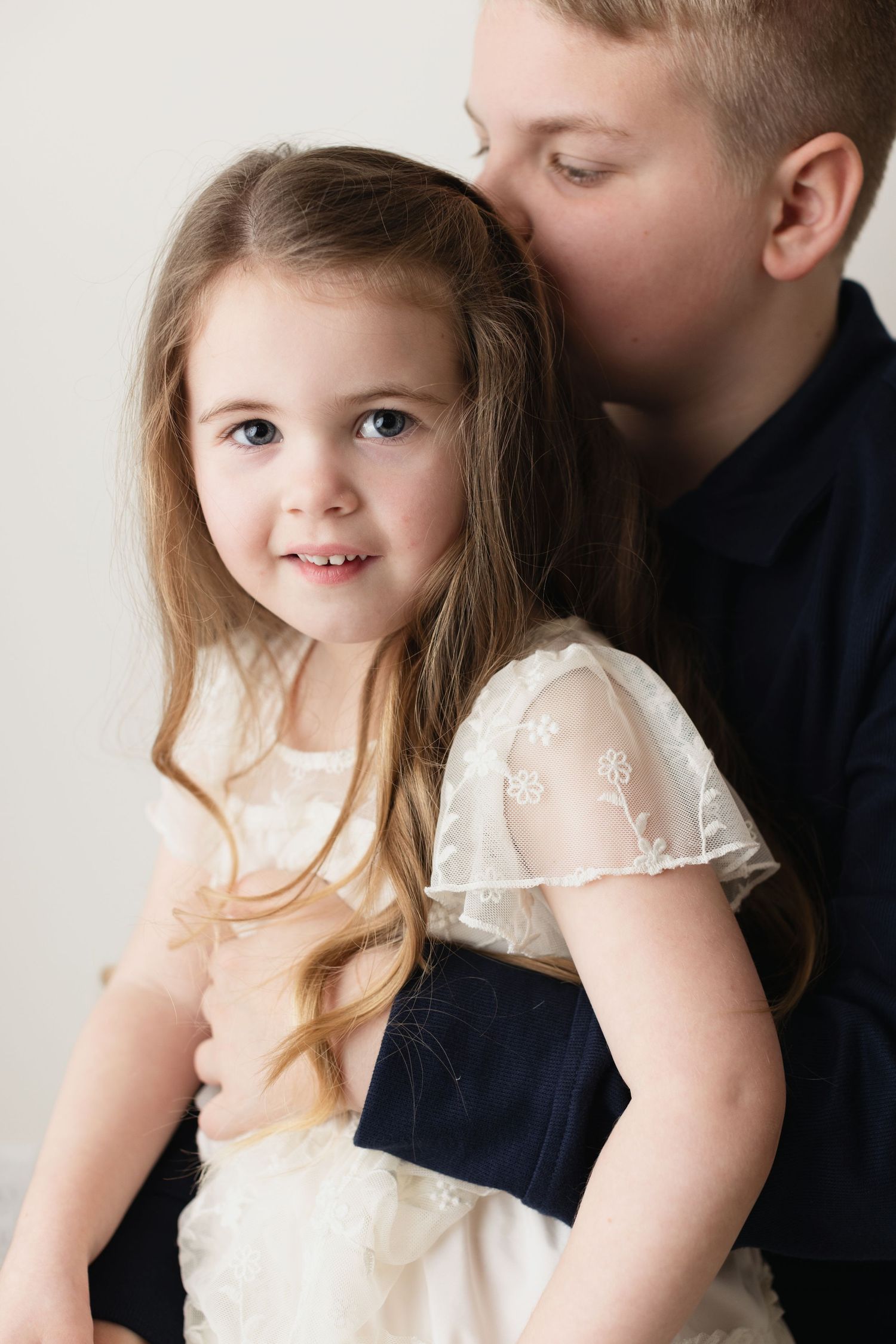 A young child in a white lace dress poses against a white background in a series of candid studio portraits.