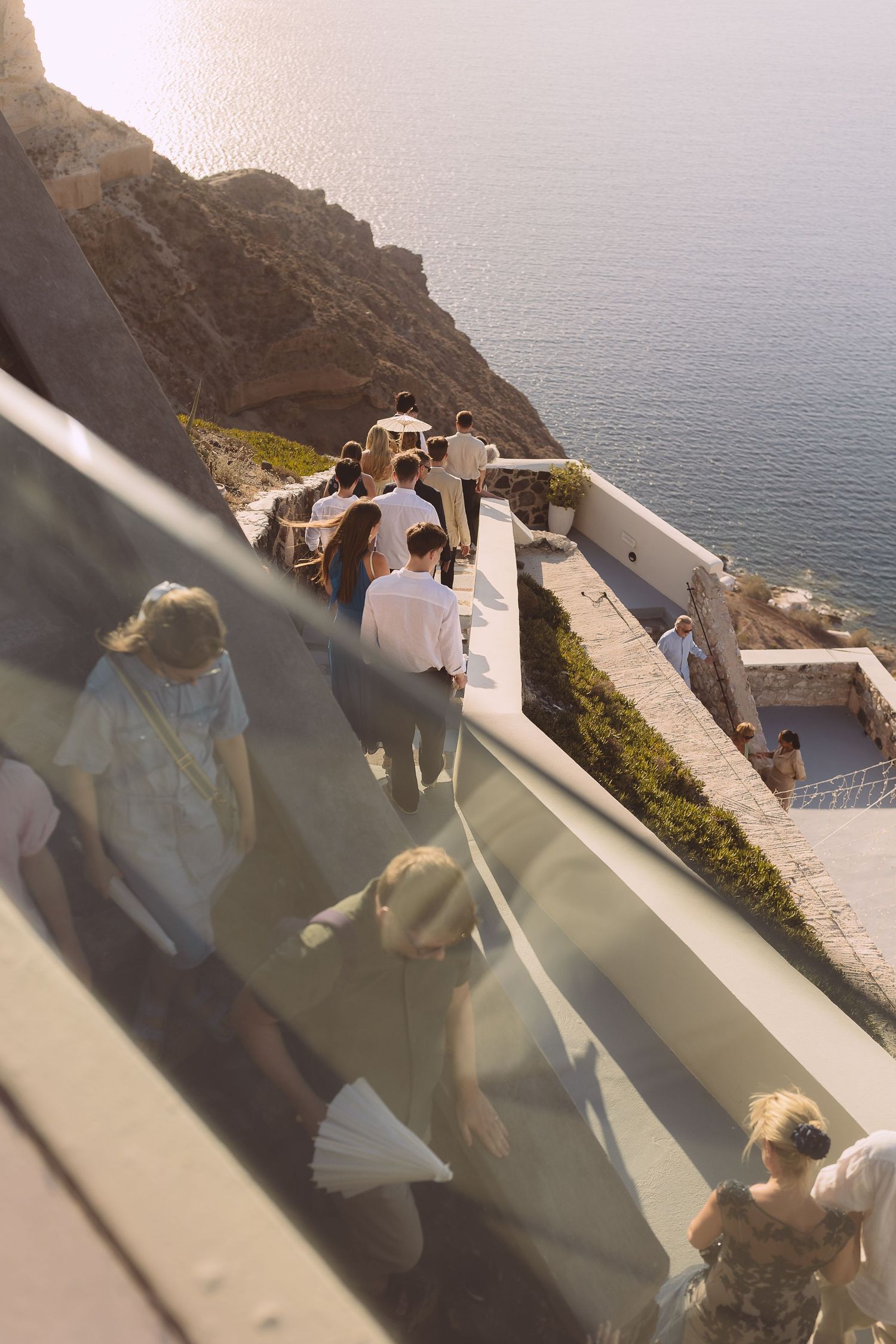 Guests at destination wedding walking down white stone steps at El Viento overlooking a scenic coastal view with blue Santorini waters.
