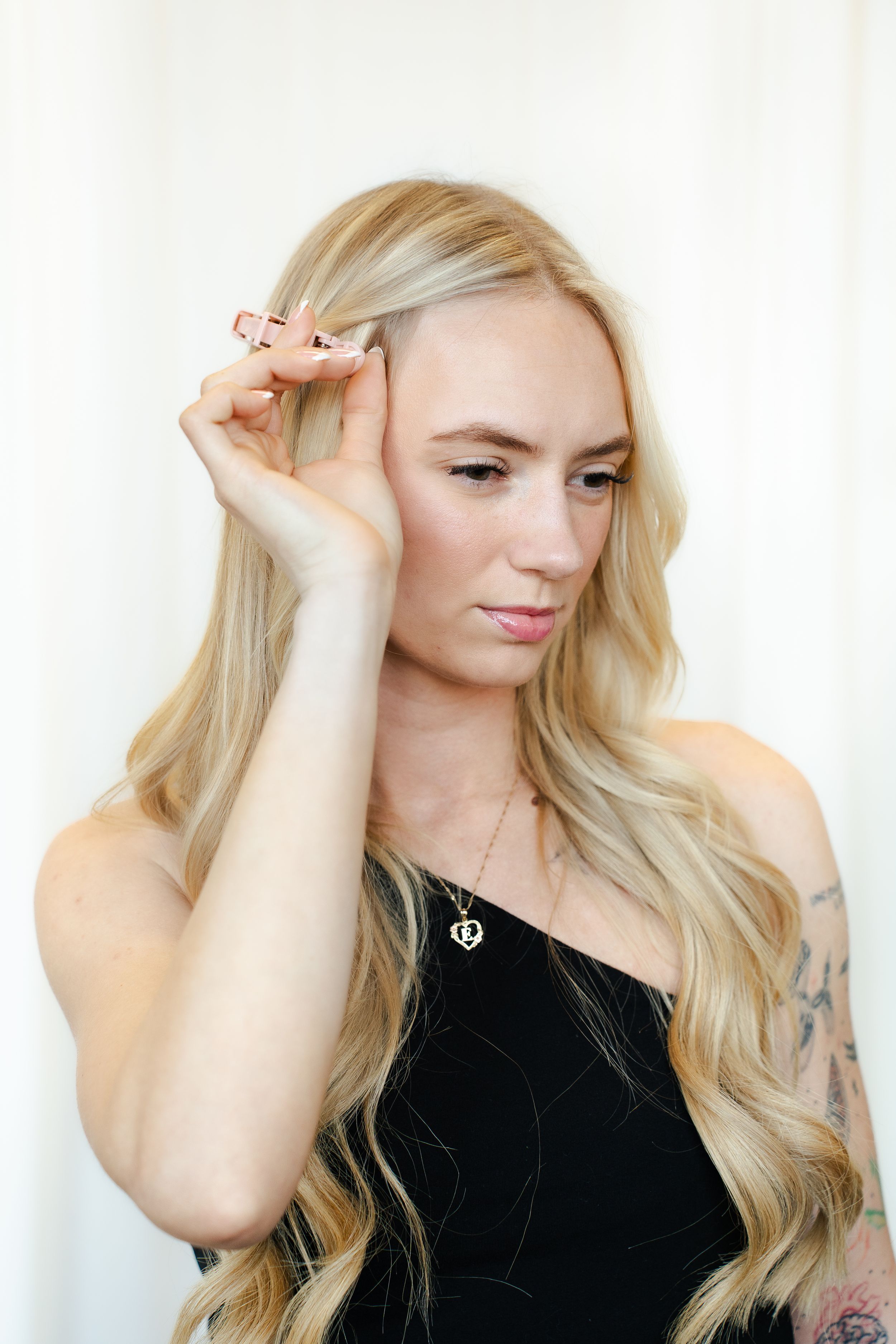 A person with long blonde wavy hair poses against a light background in a black top.