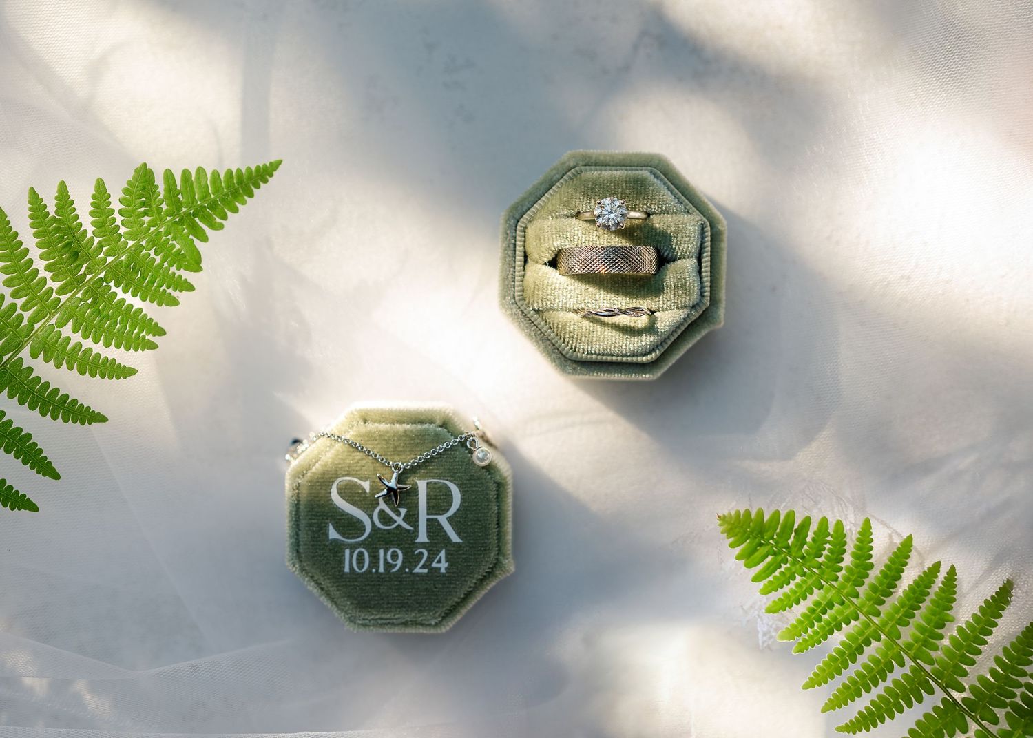 Green fern leaves frame an elegant octagonal monogram sign against a soft cloudy sky.
