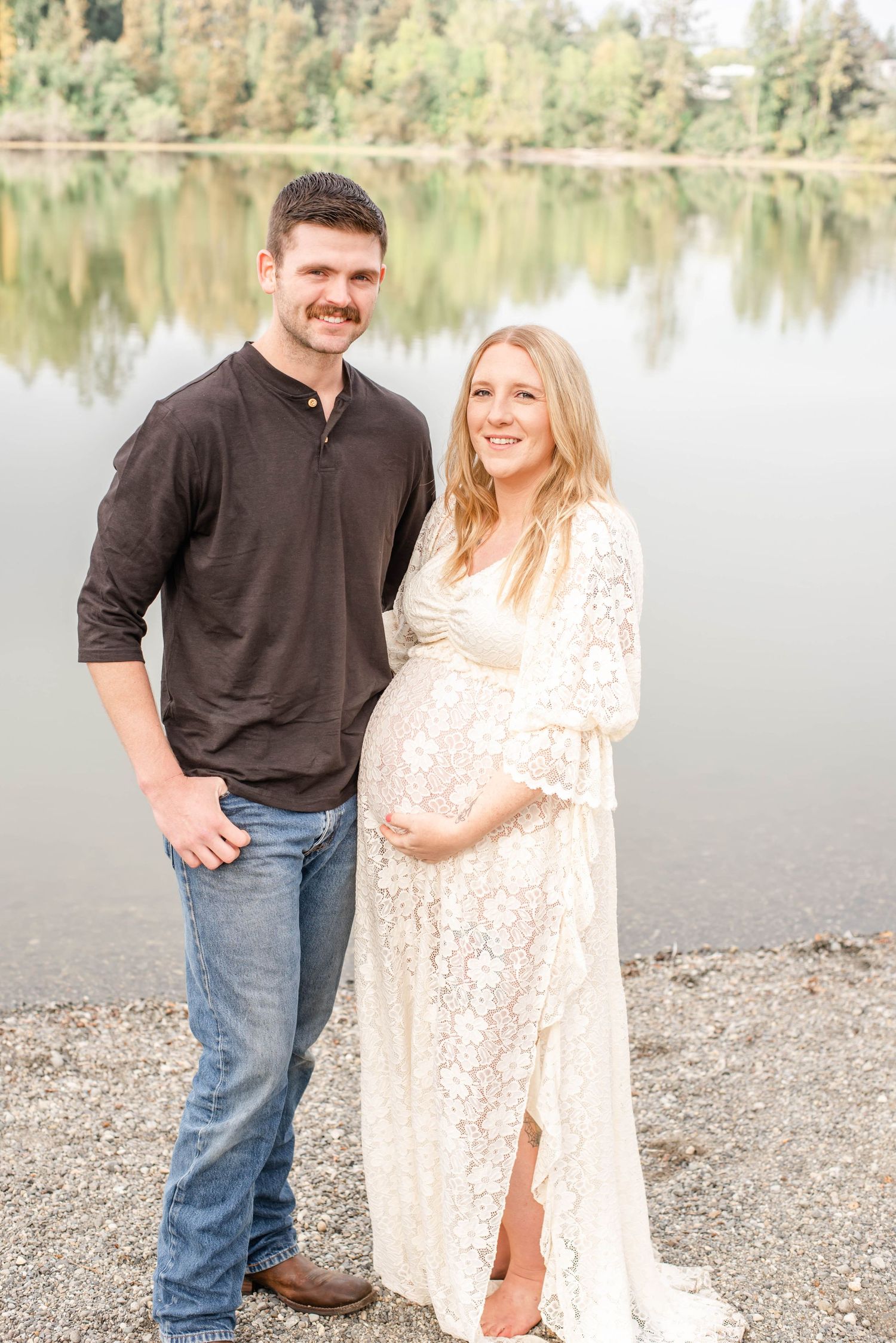 Romantic lakeside photo session with a couple in casual attire posing by the water's edge on a sunny day.