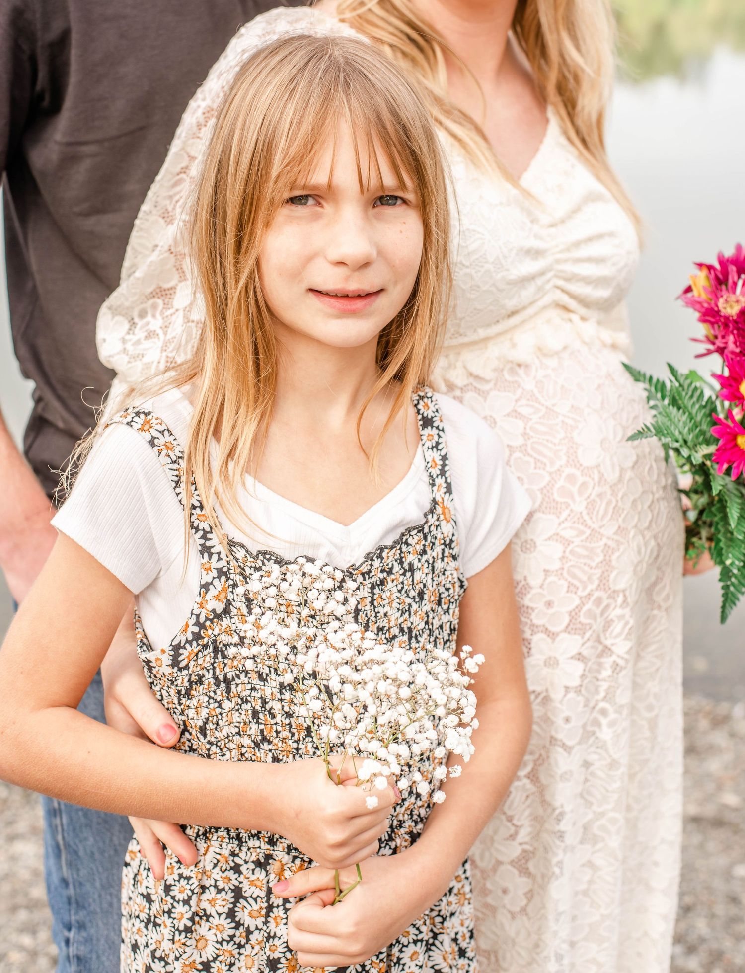 Child in a floral dress poses during an outdoor family photoshoot with bright pink flowers visible.