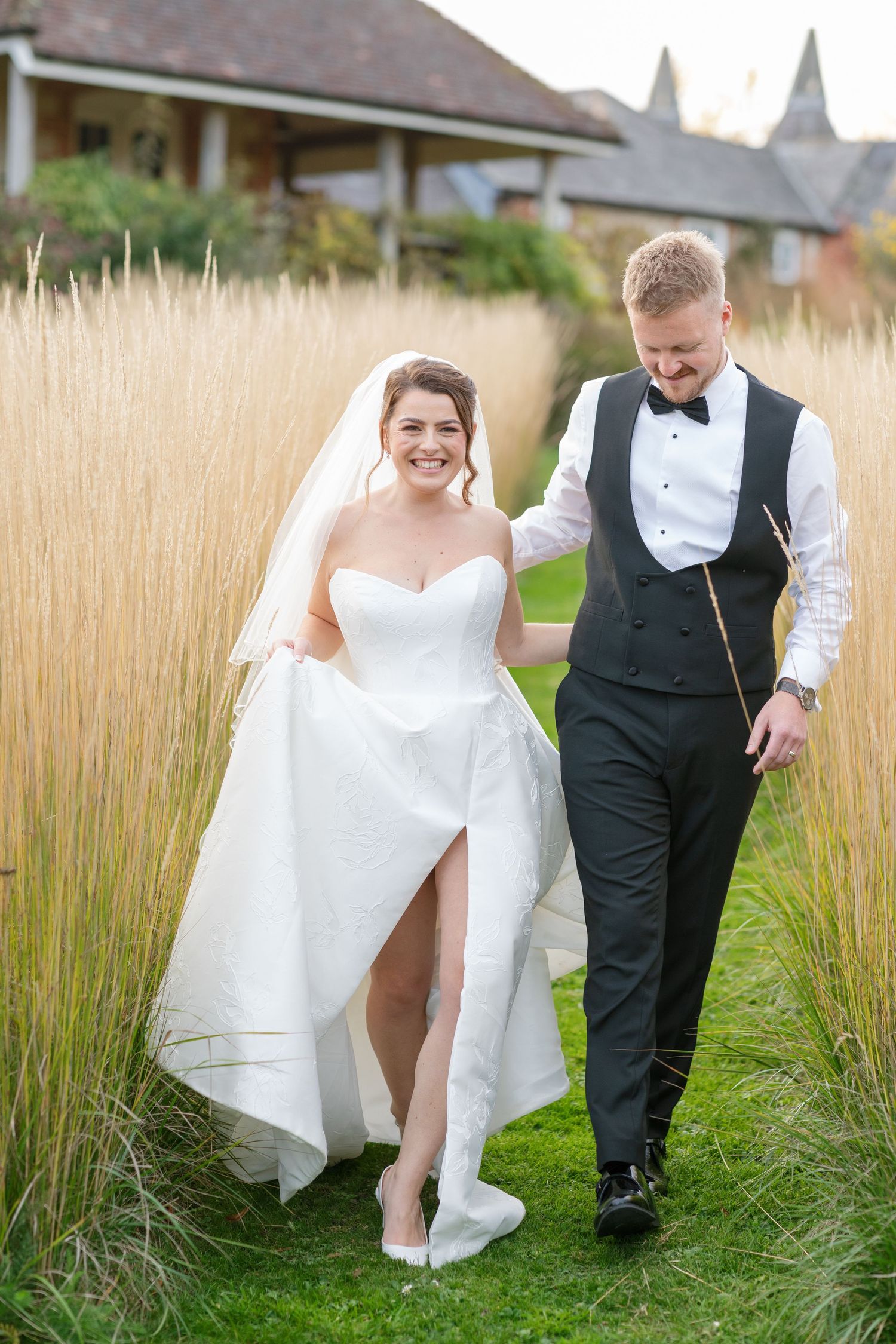 Couple walk through long grass at Bury Court Barn, photographed by Maddie Waters Hampshire wedding photographer