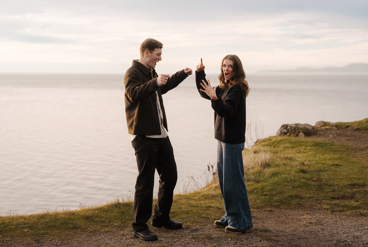 A couple shares a romantic moment on a scenic coastal cliff overlooking the ocean during sunset.