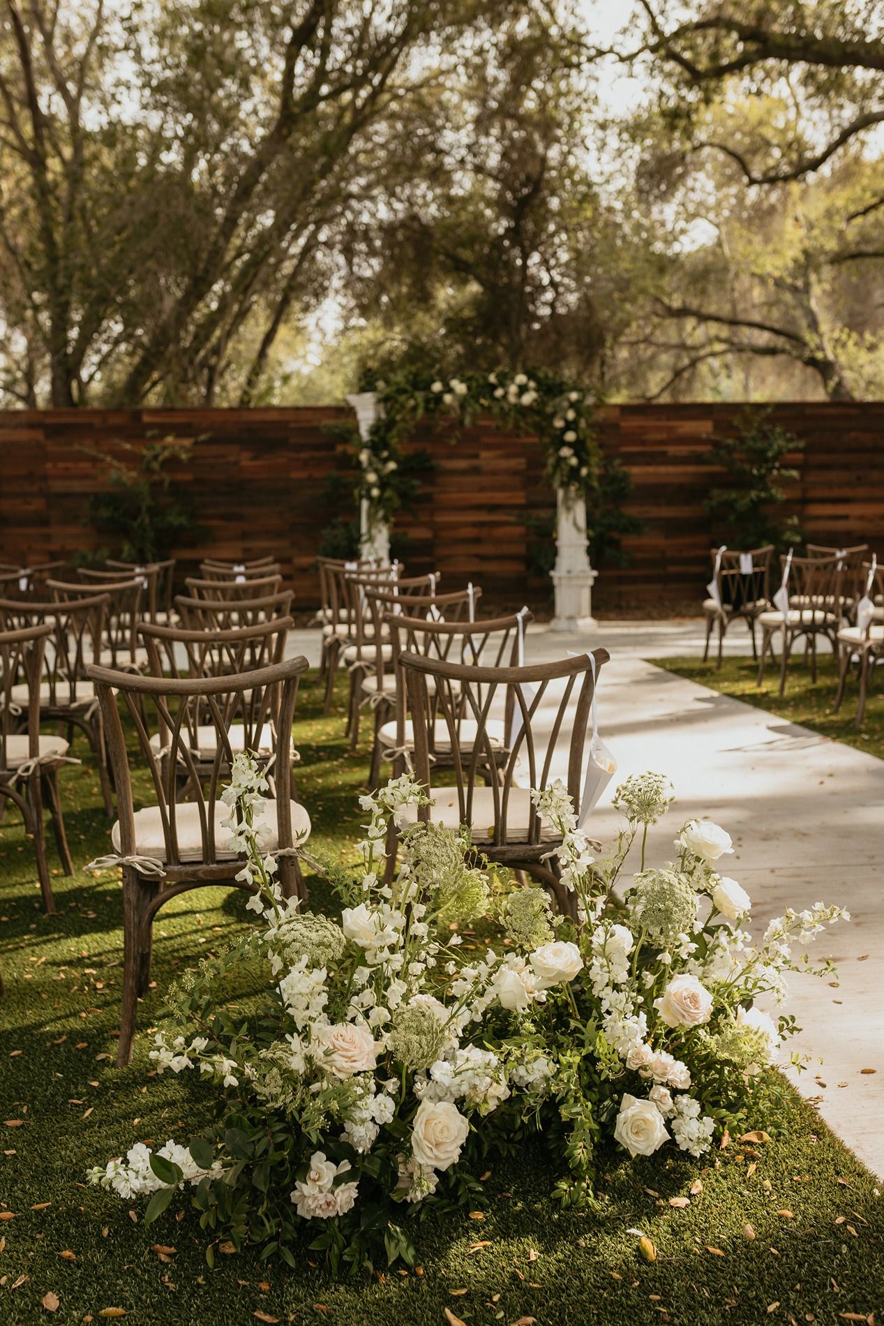Rustic outdoor wedding ceremony setup with wooden chairs and white floral arrangements along a stone pathway at The Oaks at Duncan Lane.