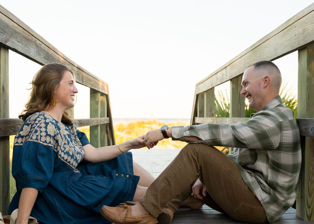 A couple sits together on a wooden deck overlooking a scenic landscape during sunset.