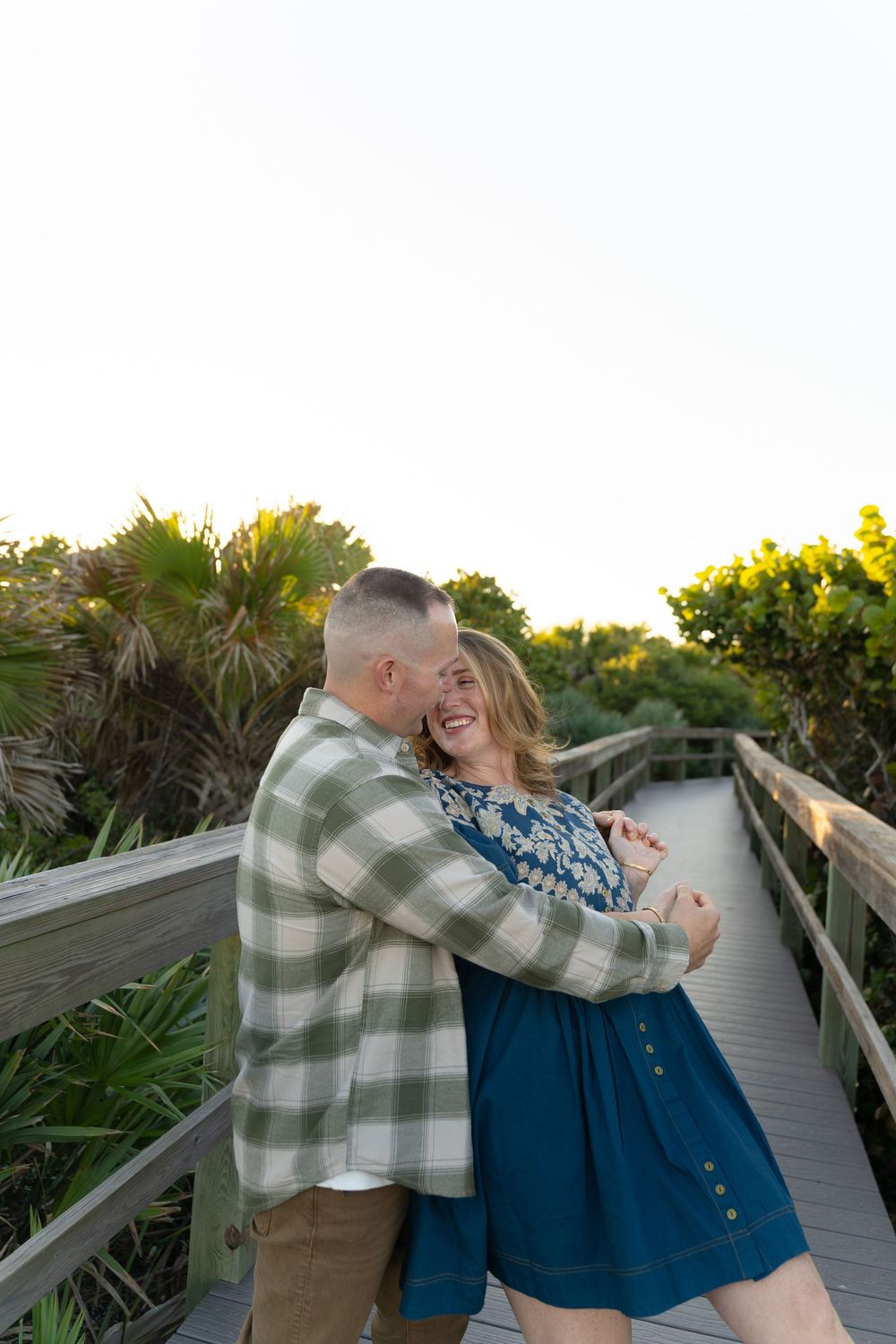 Couple dancing and laughing together on wooden boardwalk during sunset.