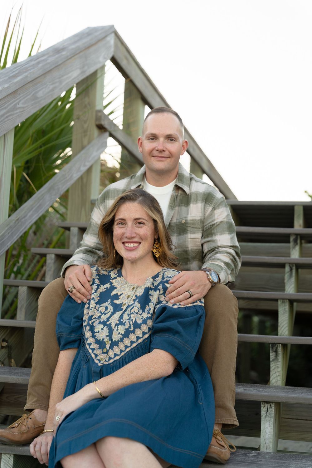 Romantic couple embracing on wooden boardwalk during sunset photoshoot at the beach.
