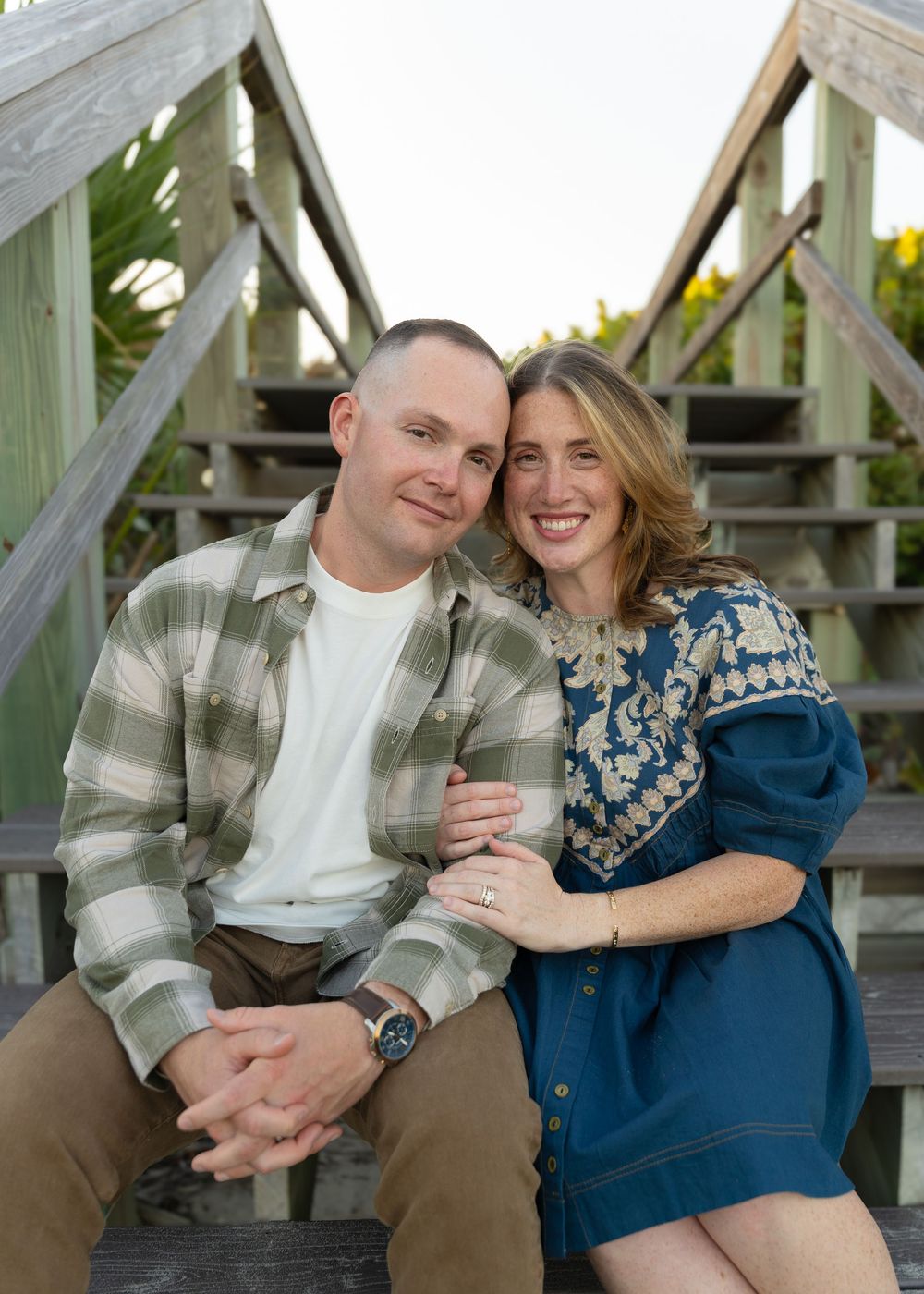 Romantic couple sitting together on wooden boardwalk during sunset wearing casual attire.