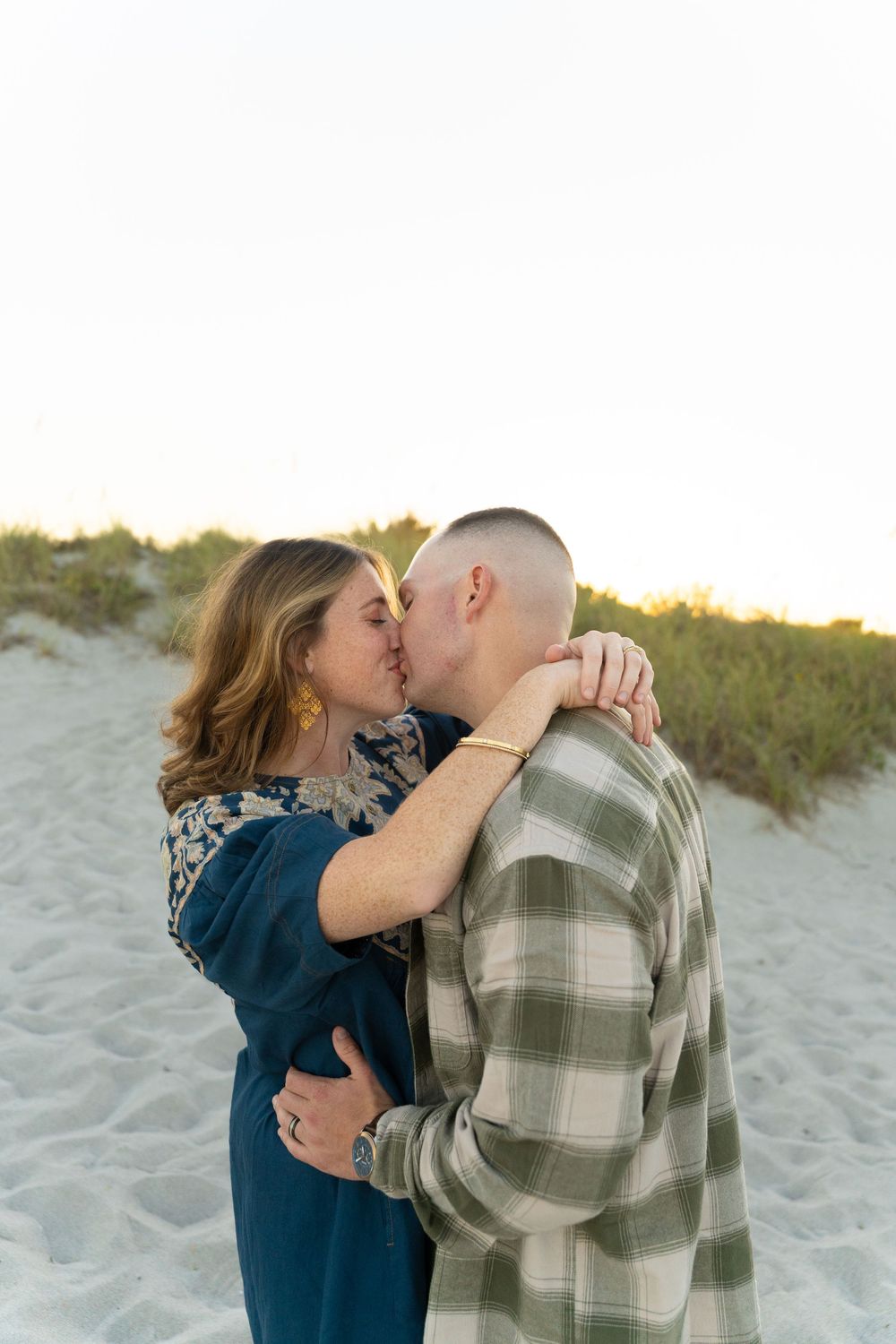Intimate couple sharing tender moments on beach sand during golden hour.