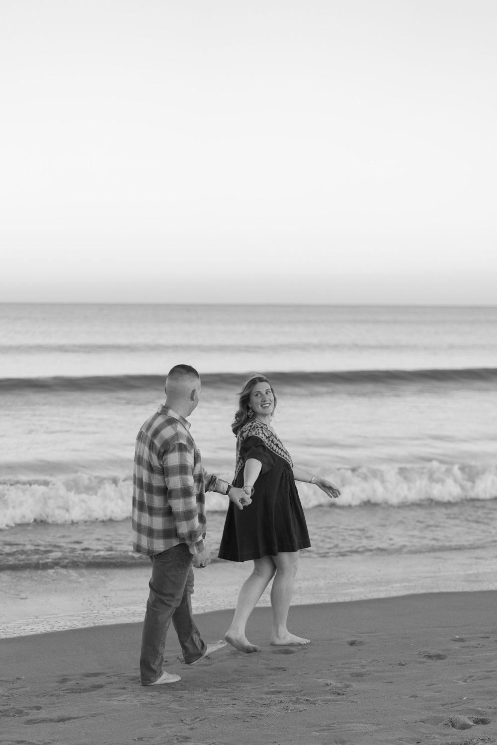 A couple shares a romantic moment on the beach at sunset as waves roll in along the shoreline.