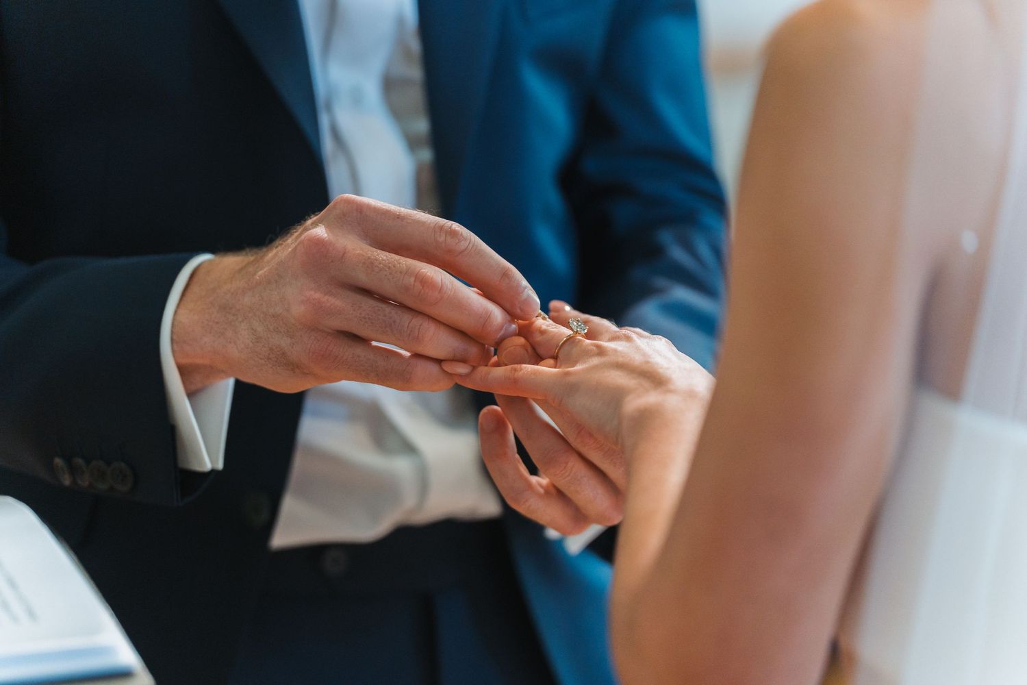 A couple signs marriage documents at a wedding ceremony with hands visible holding pens on official paperwork.