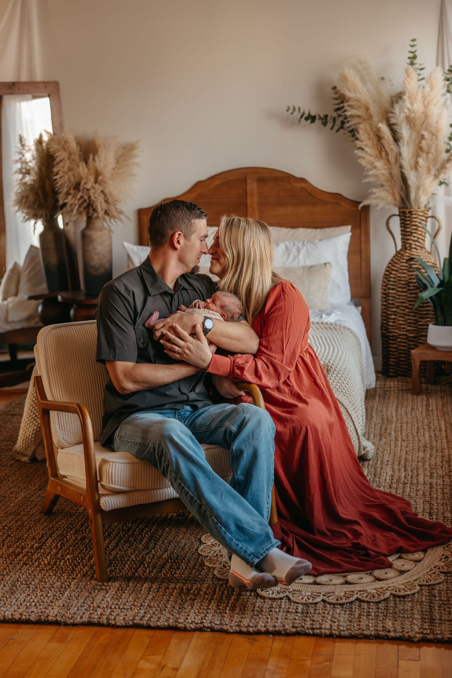 Romantic couple in casual attire sharing intimate moments on a woven rug with pampas grass decor in warm lighting.
