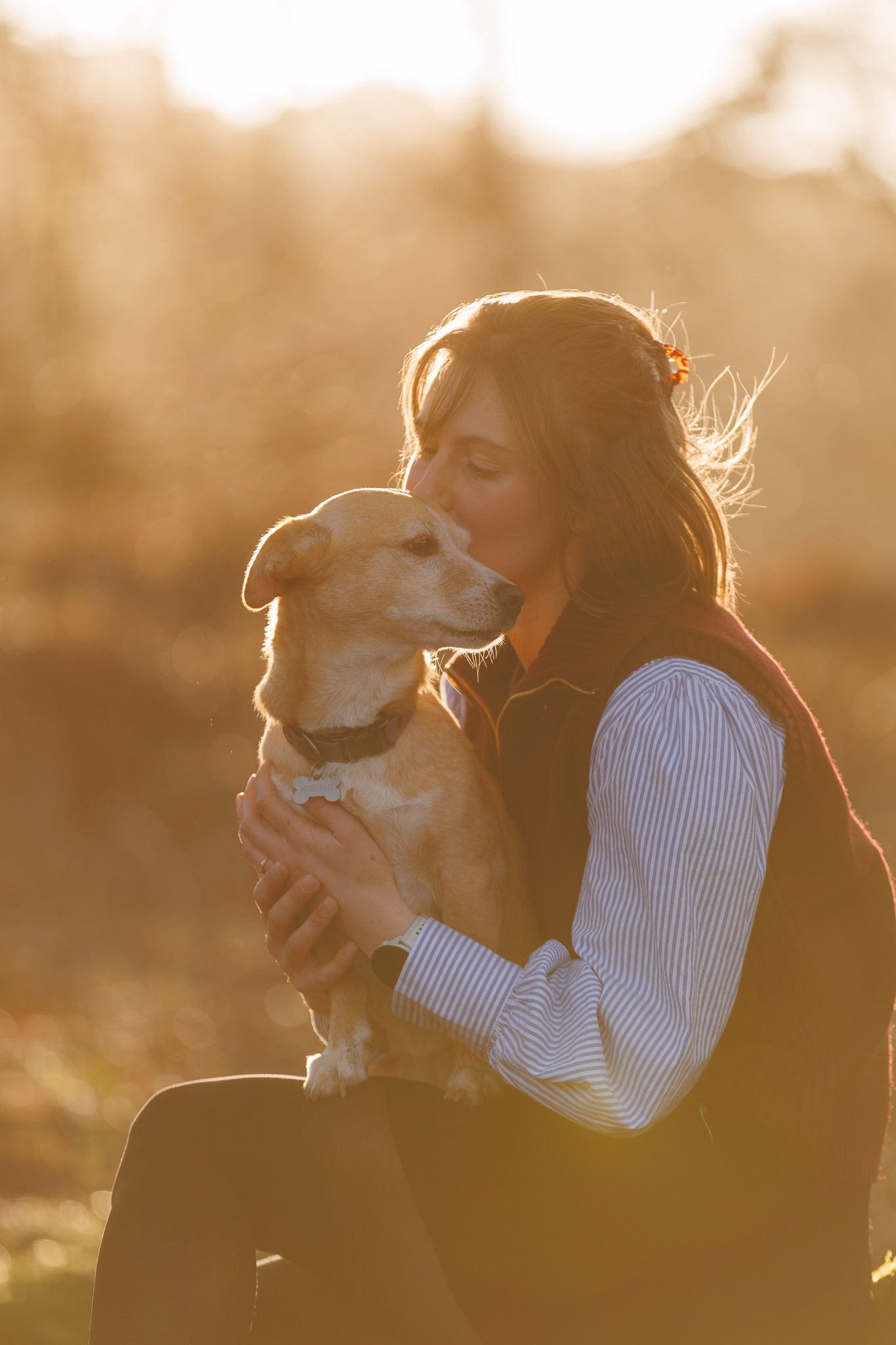 A brown horse and rider in a white sweater pose together against autumn foliage in soft natural lighting.