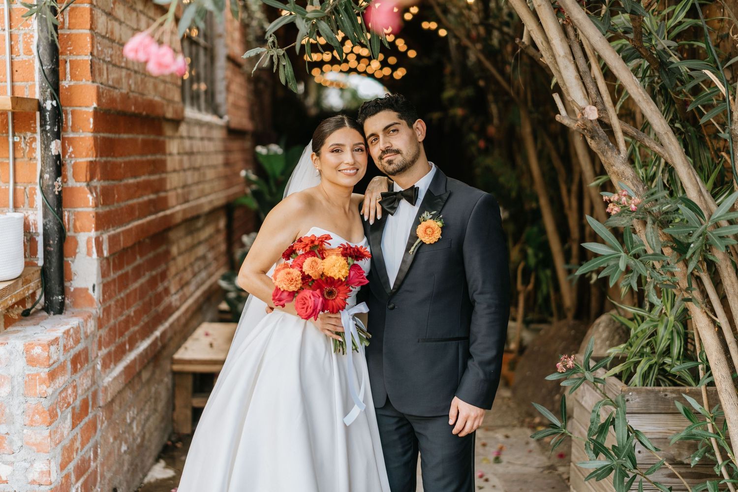 Ruby and Sina smiling together during wedding portraits beside a brick walkway.