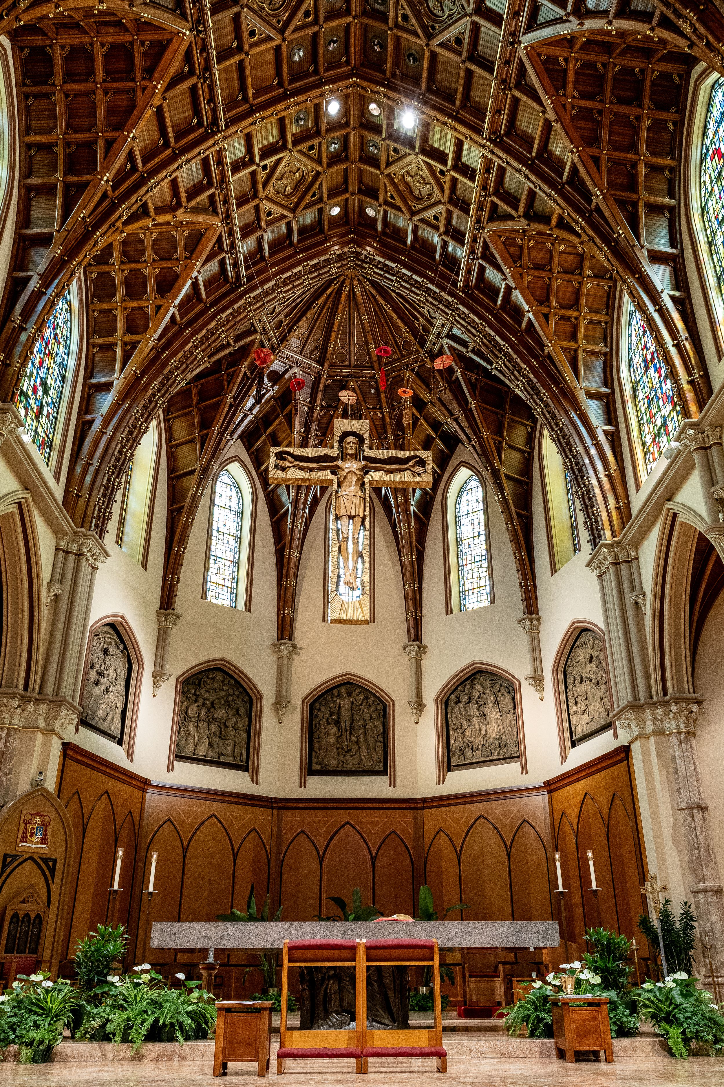Interior of a Gothic church with ornate wooden vaulted ceiling, stained glass windows and crucifix at the altar.