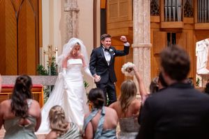 A wedding ceremony takes place inside an ornate church with wooden pews and decorative columns.