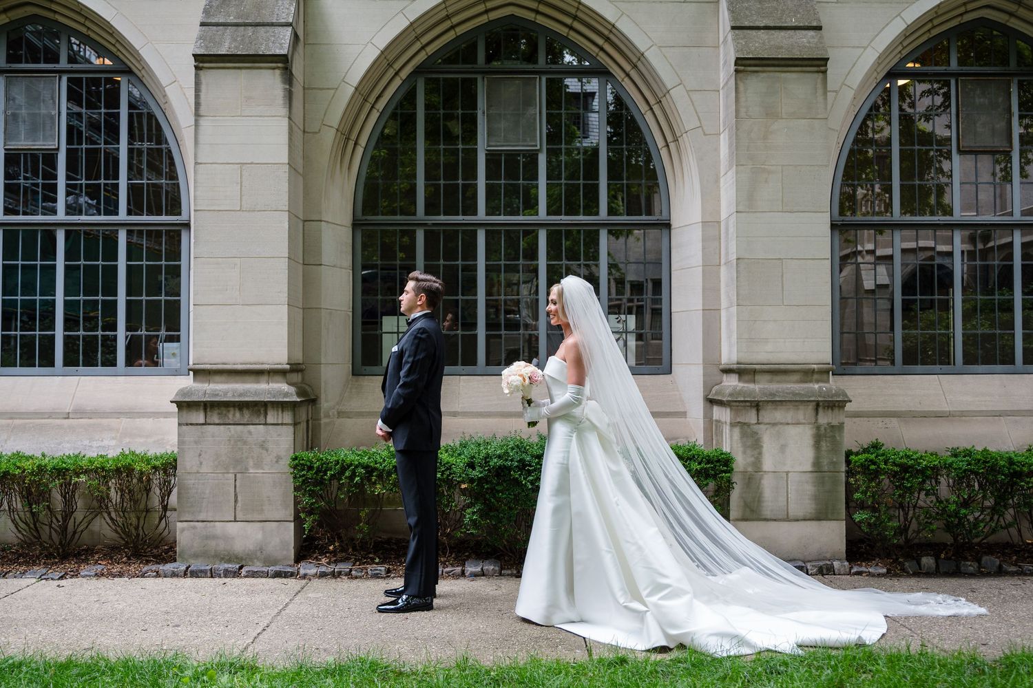 A wedding couple walks through an elegant stone archway corridor with gothic architectural details.