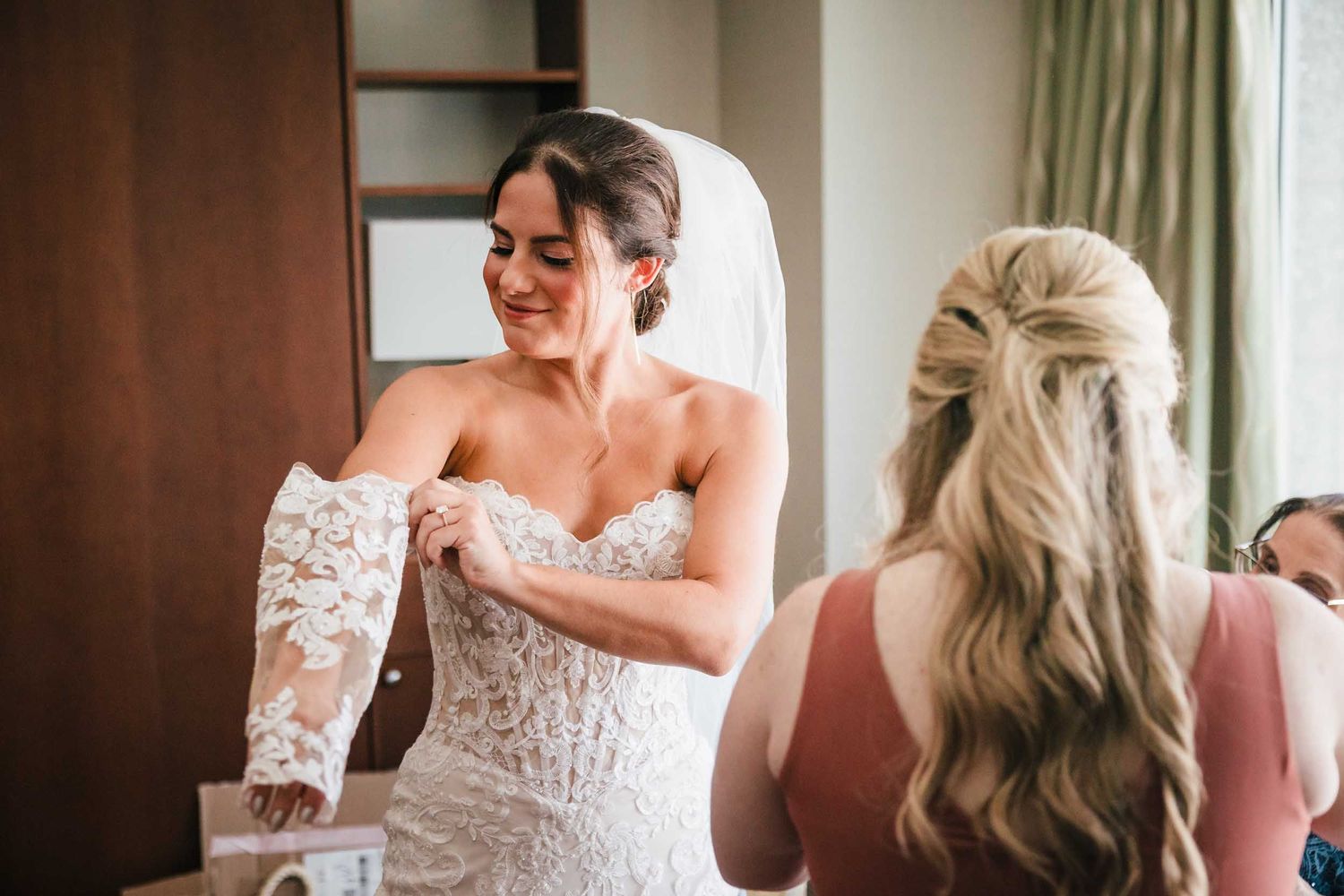 Bride putting on lace sleeves over her wedding dress during wedding morning preparations in Boston
