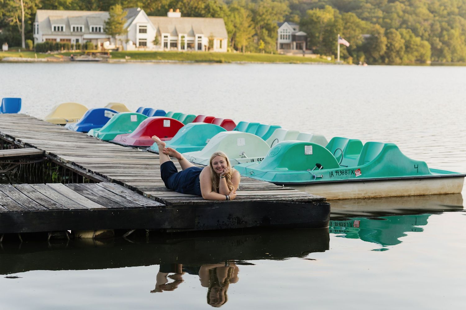 Colorful pedal boats and kayaks lined up along a wooden dock at a scenic lake during summer.