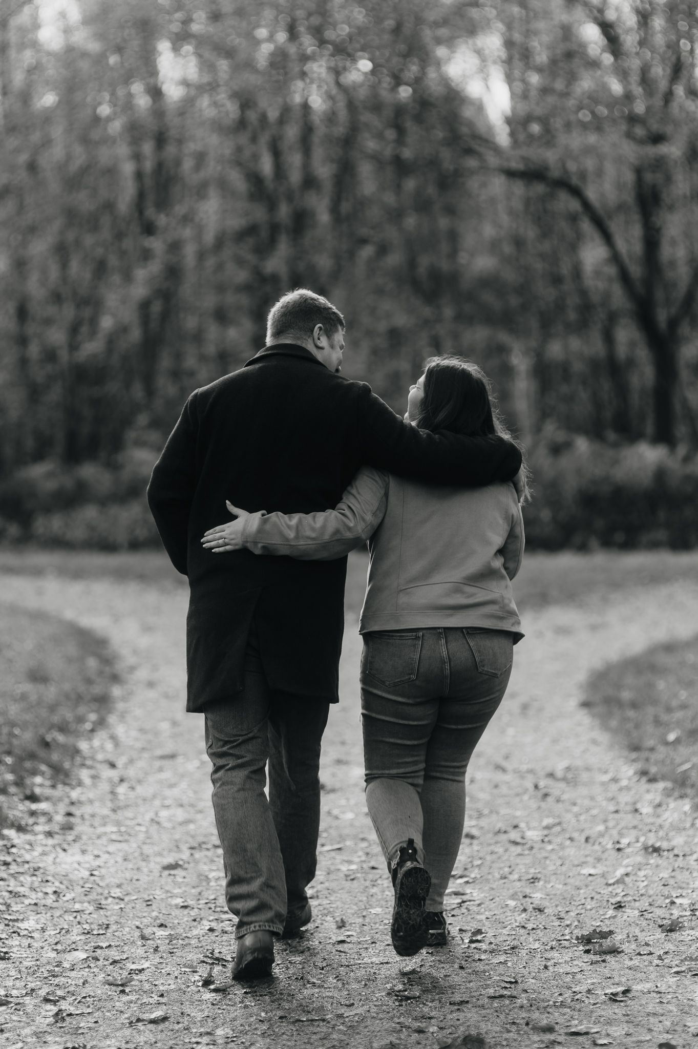 Black and white photo sequence showing two people walking together arm in arm down a gravel path through the woods.