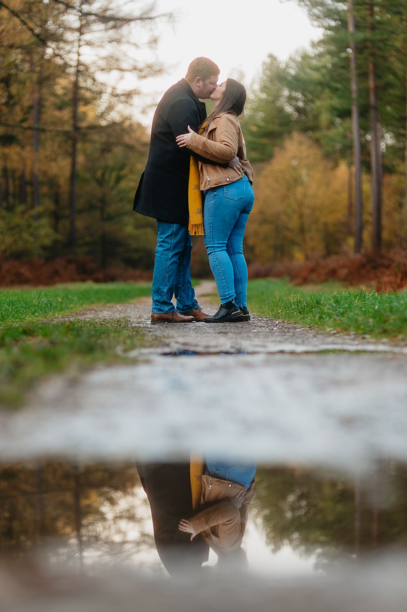 A romantic couple shares a tender moment on a forest path with puddle reflections in autumn.