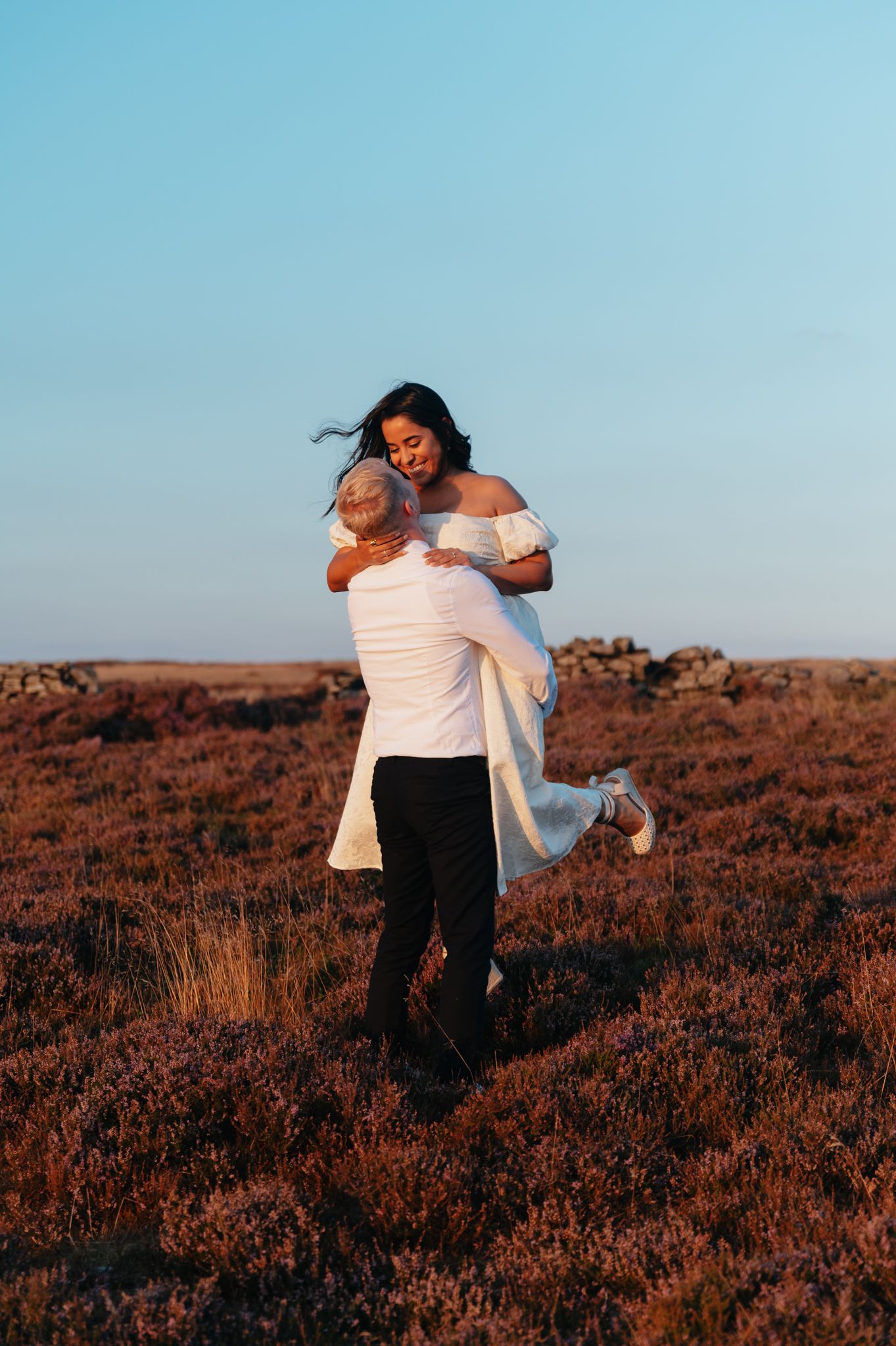 A couple embraces in a romantic moment on a heathered hillside during golden hour.