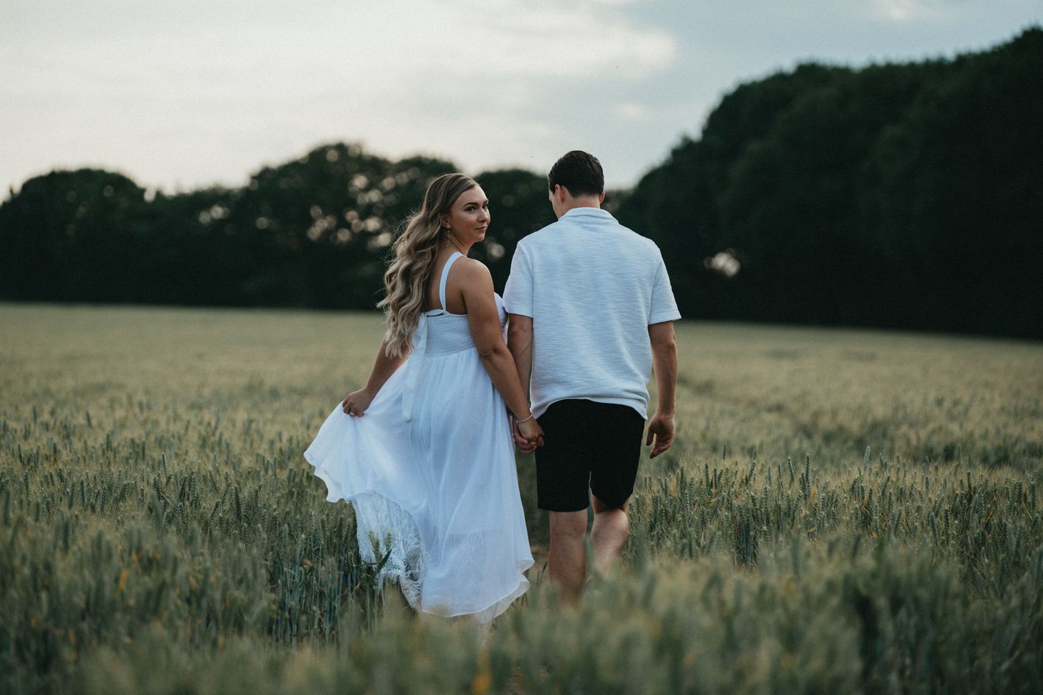 Romantic couple embraces while standing in a golden wheat field during sunset.