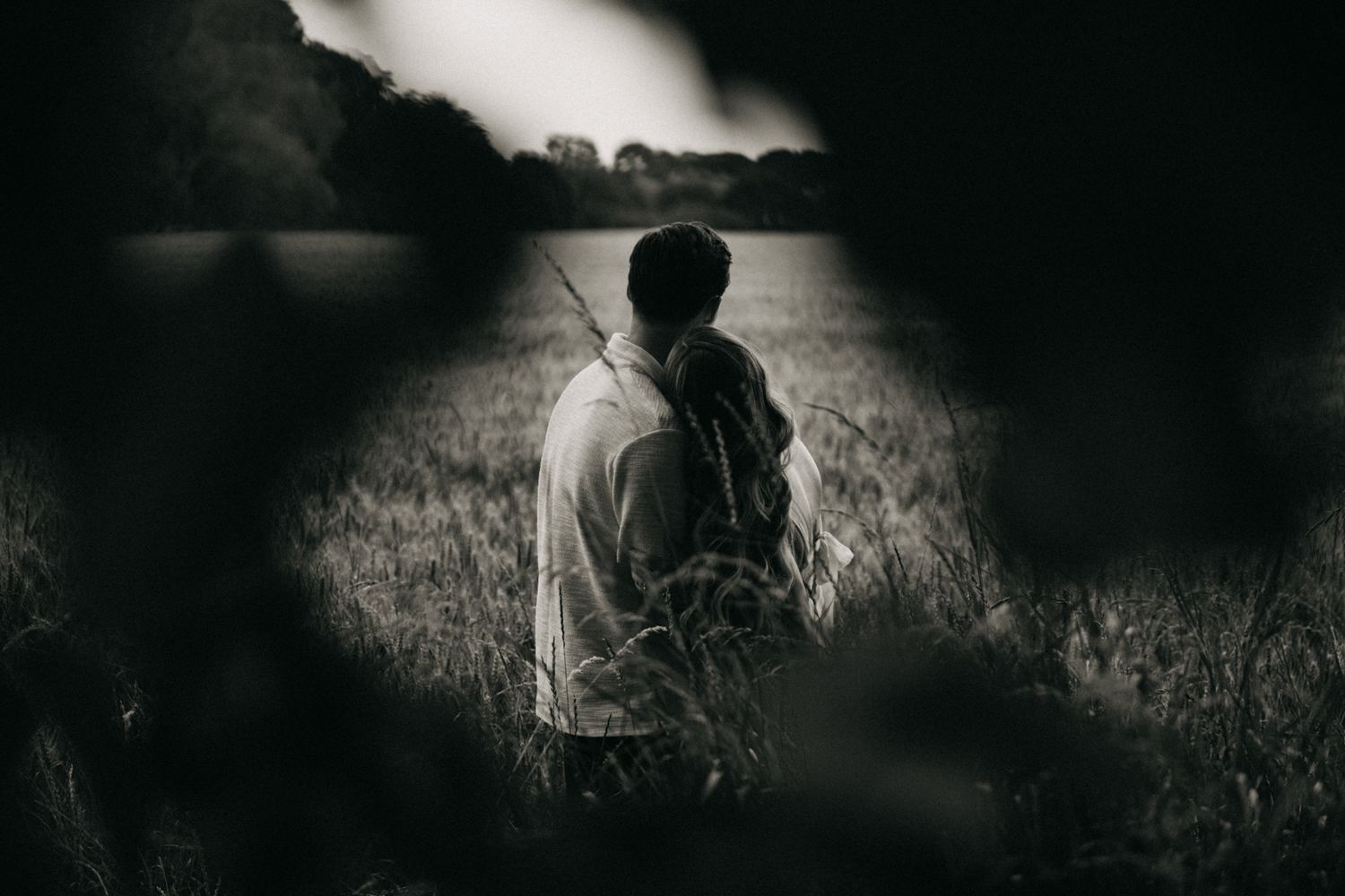 A dark and moody black and white landscape photograph with silhouettes in a field at dusk.