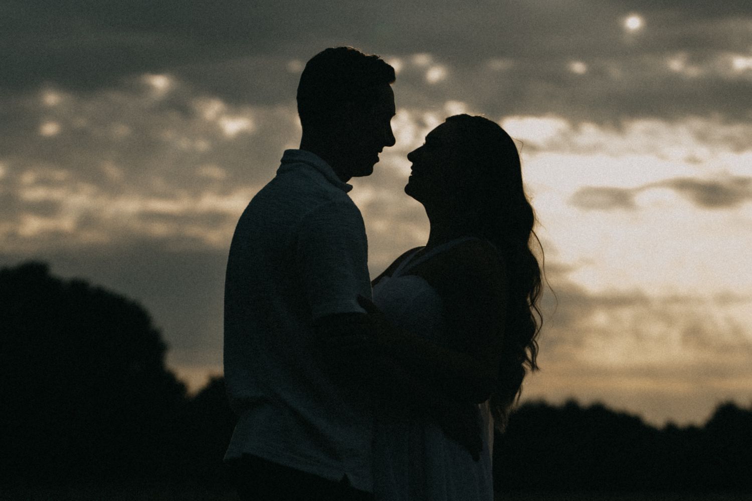 Silhouettes of a couple embracing against a dramatic sunset sky with clouds in the background.
