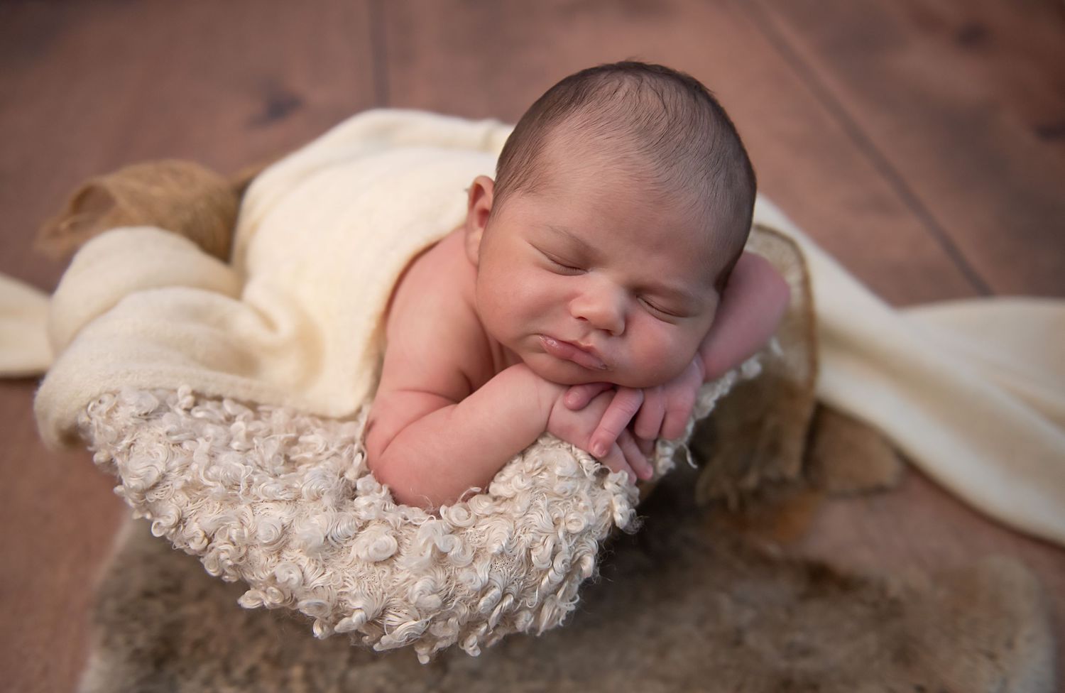 A sleeping newborn baby wrapped in delicate lace fabric lies peacefully on a soft beige blanket.
