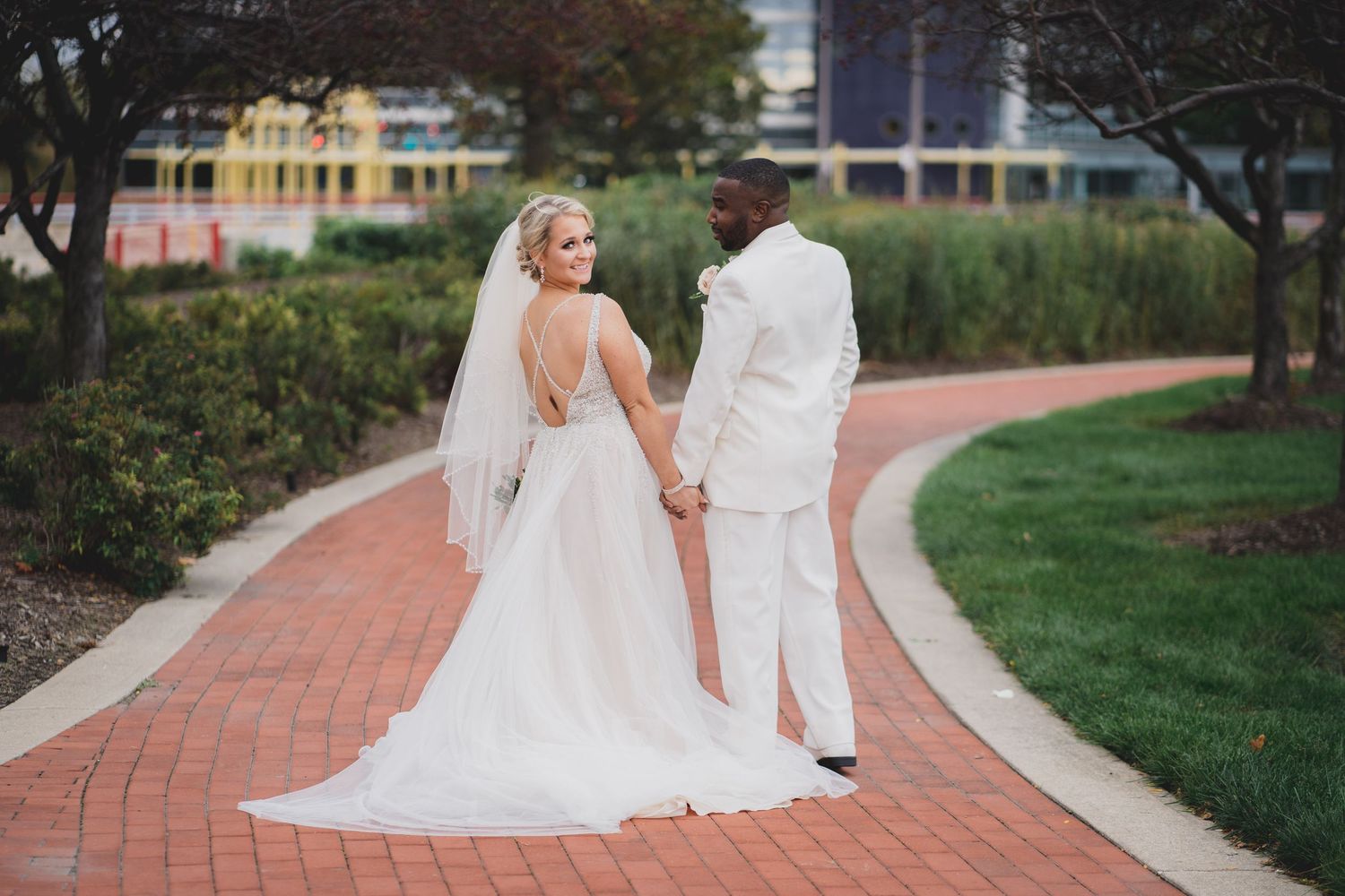 Wedding couple walking along a curved brick pathway through a garden setting.