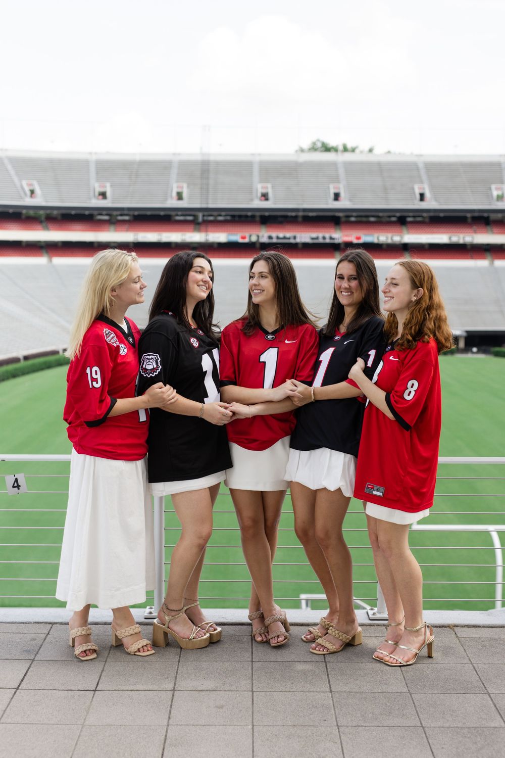 Group photo of graduates wearing red jerseys and white skirts posing at sports stadium.