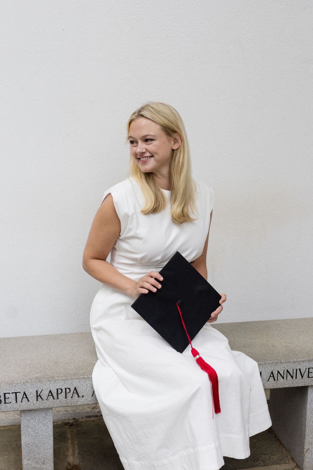 Graduate in white dress poses with graduation cap against white columns in creative photo sequence.