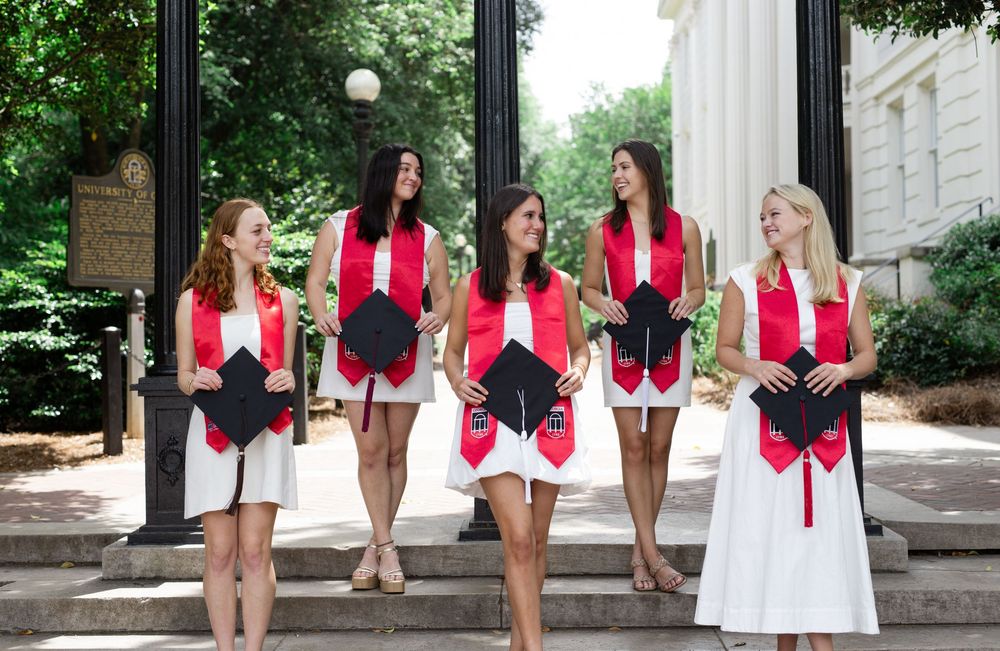 A sequence of graduates in red and white attire walking and posing on stone steps during a graduation ceremony.