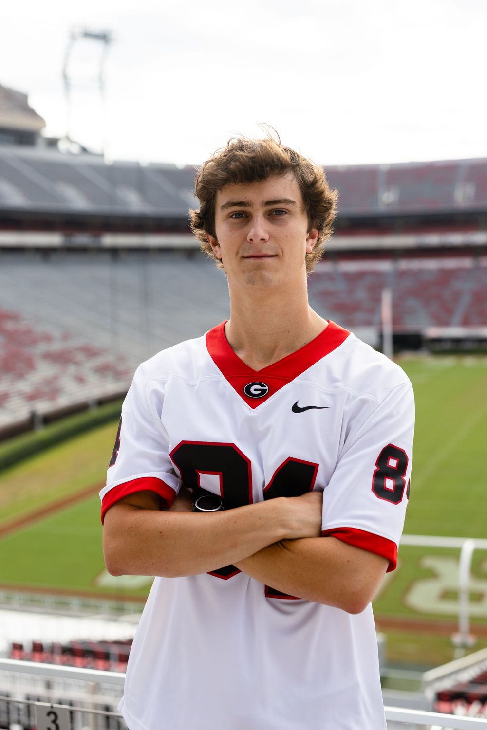Football player in white University of Georgia jersey poses in empty stadium.