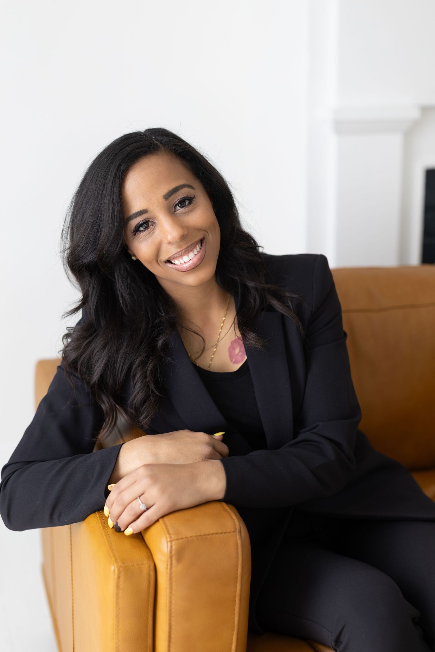 Professional in black blazer lounges on mustard yellow couch in bright modern office setting.