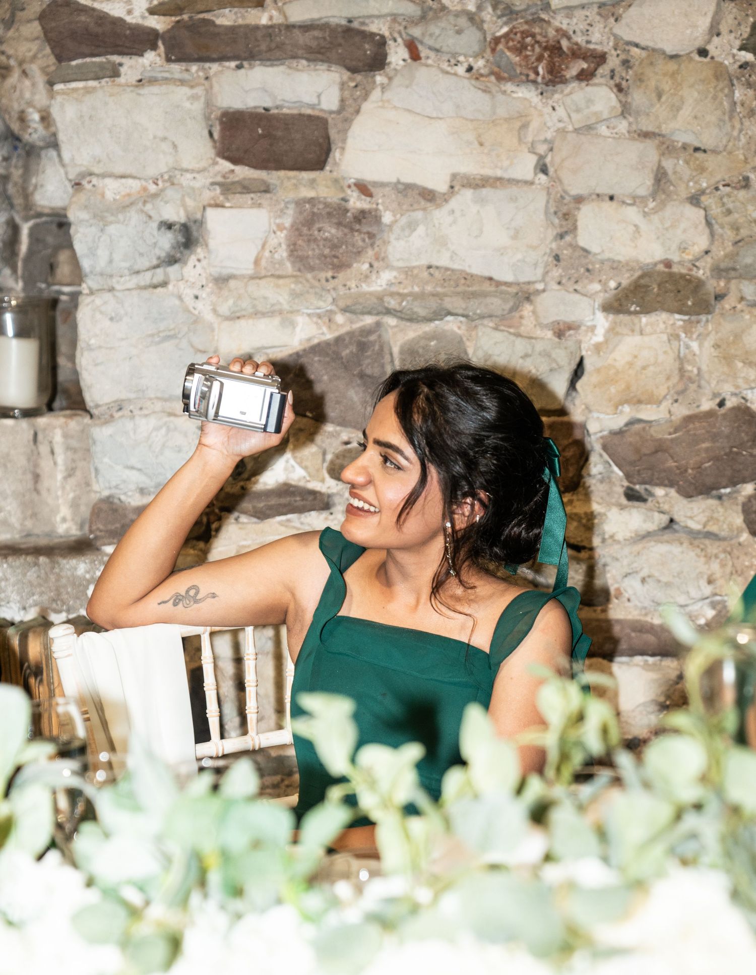 Someone enjoying a drink against a rustic stone wall backdrop with greenery in the foreground.