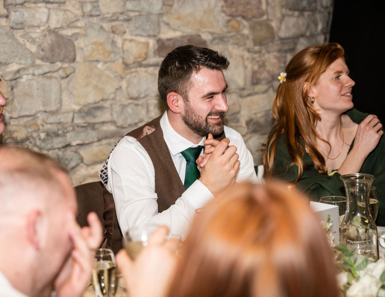 Guests laughing and socializing at an elegant stone-walled wedding reception venue with decorative lighting.