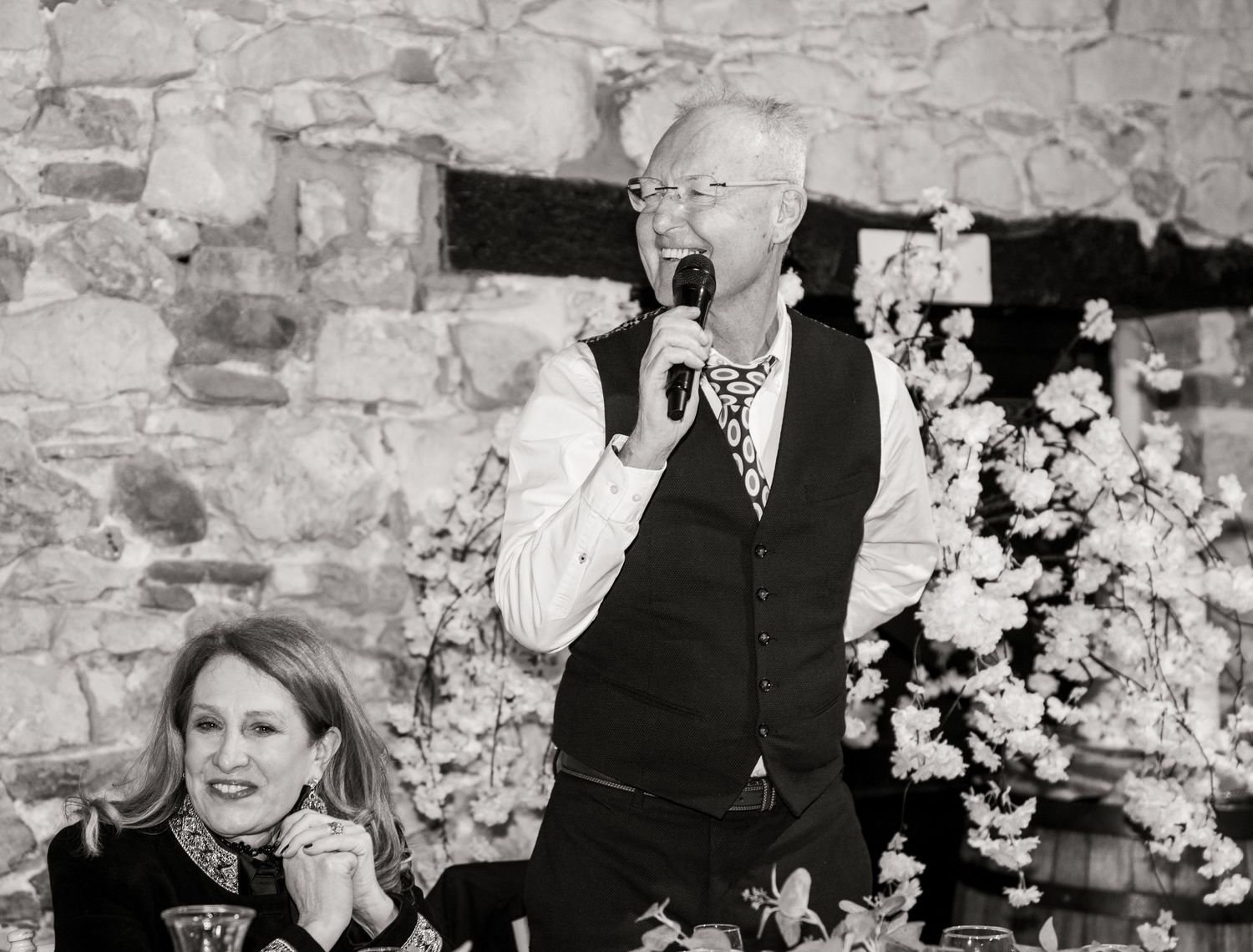 Black and white candid photos of wedding guests enjoying a reception at a rustic stone venue.