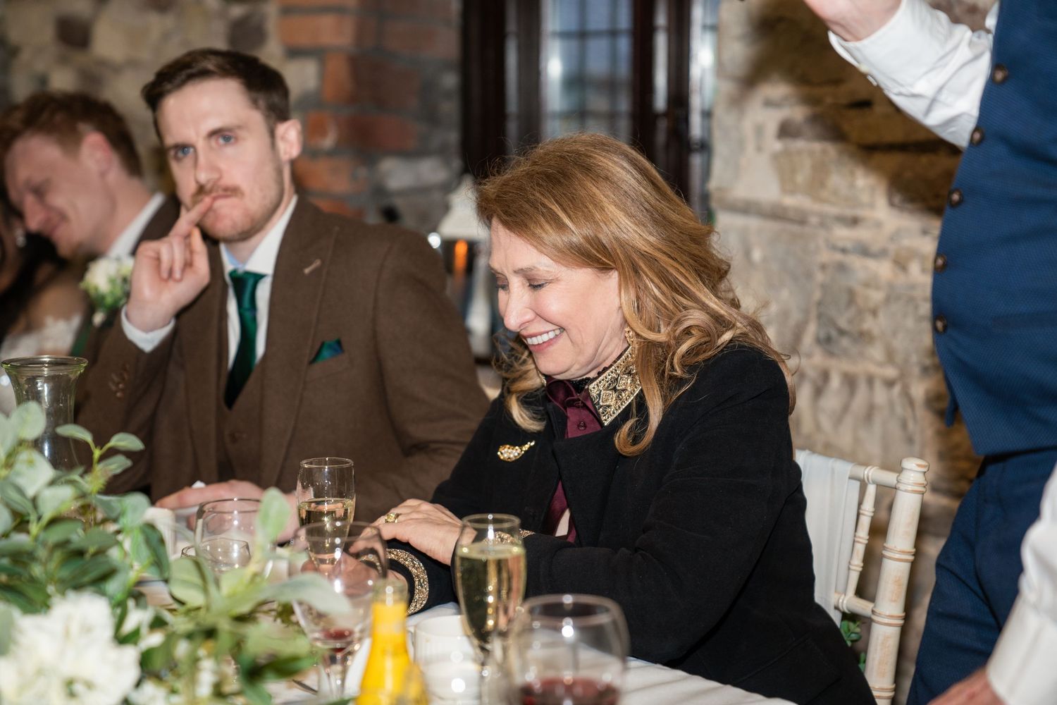 Wedding guests socializing and dining at long tables in a rustic brick and stone venue.