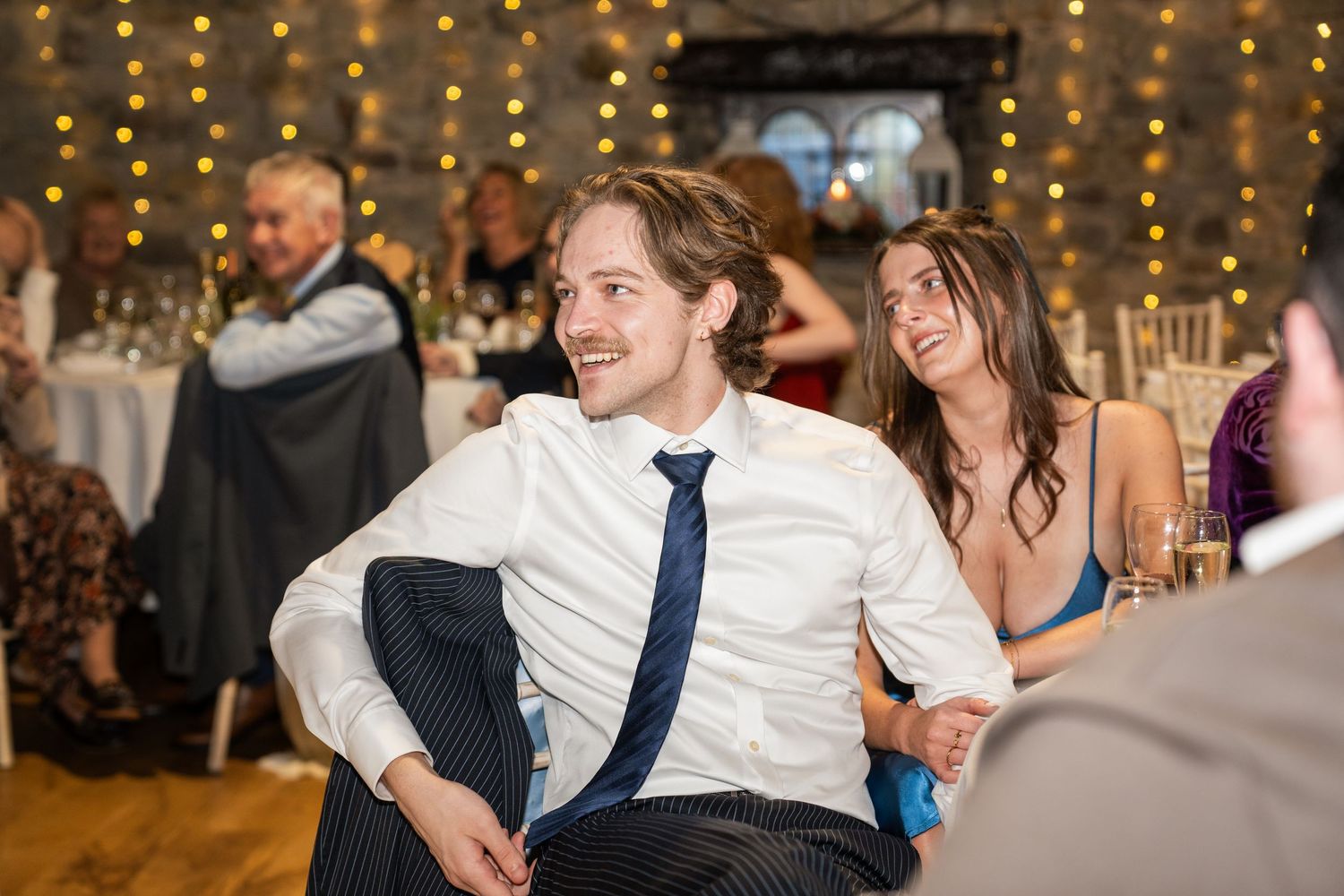 Wedding guests dance and celebrate on the dance floor under warm twinkle lights at a reception venue.