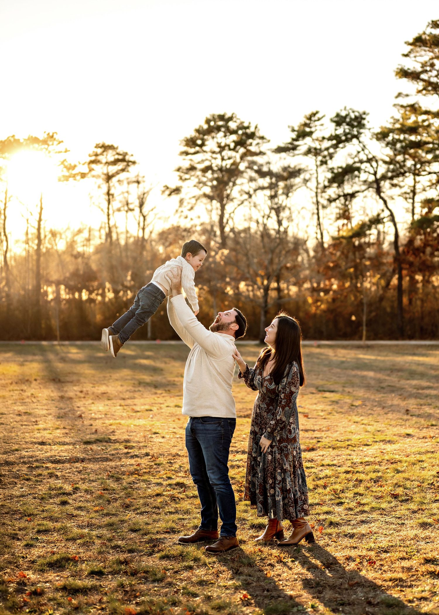 A couple dances together in a golden sunlit field at sunset with tall pine trees in the background.