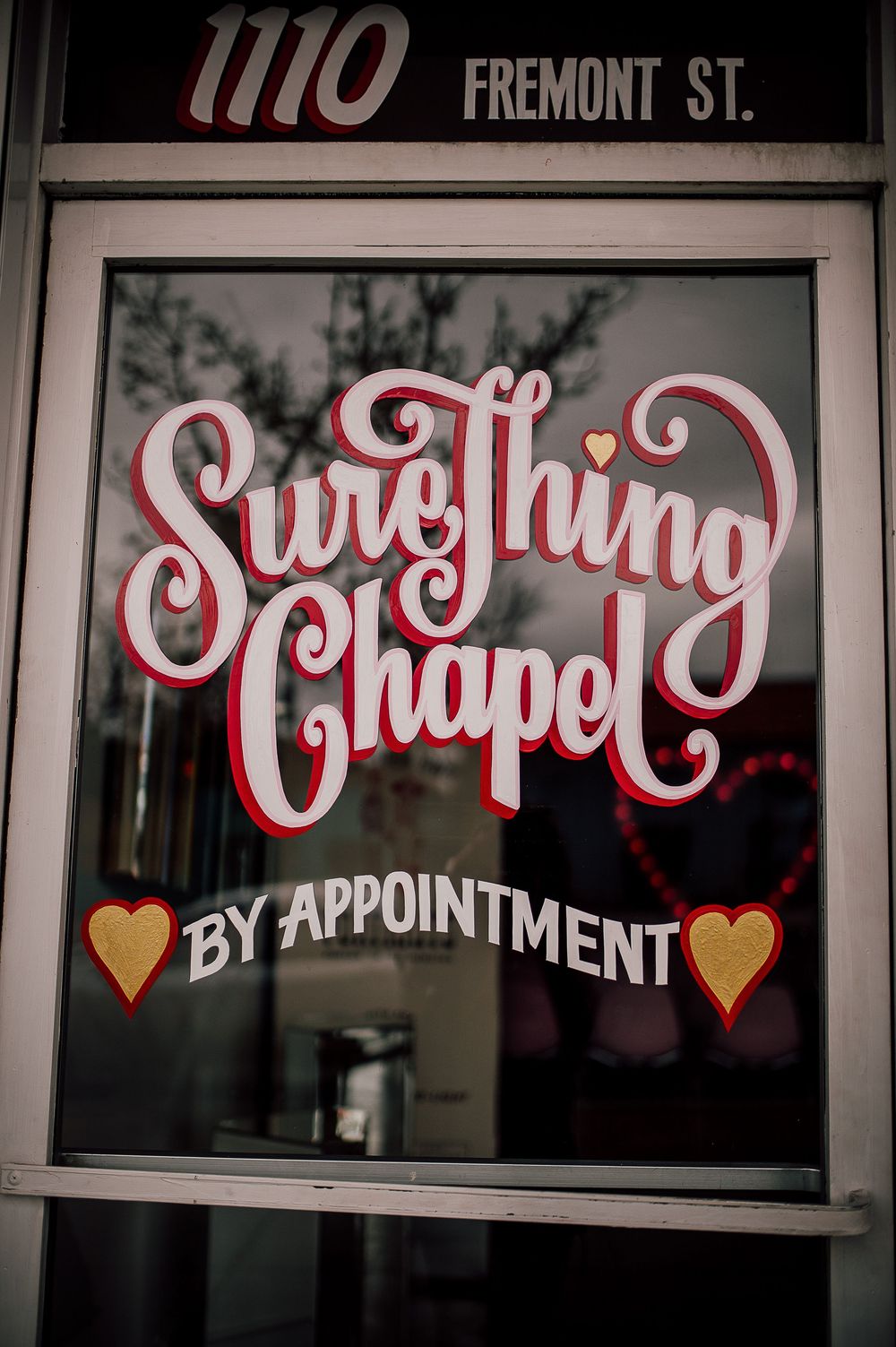 Vintage-style window signage showing 'By Appointment' text with decorative hearts and lettering on dark glass.