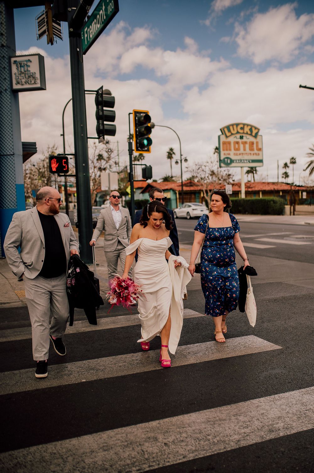Wedding party walks along a Las Vegas sidewalk with vintage signage and palm trees in the background.
