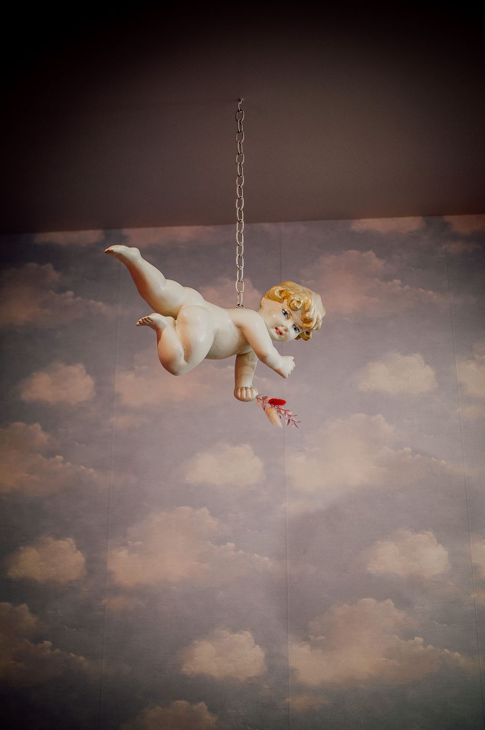 Artistic photo sequence of a cherub or baby doll figure floating against a cloudy sky background.