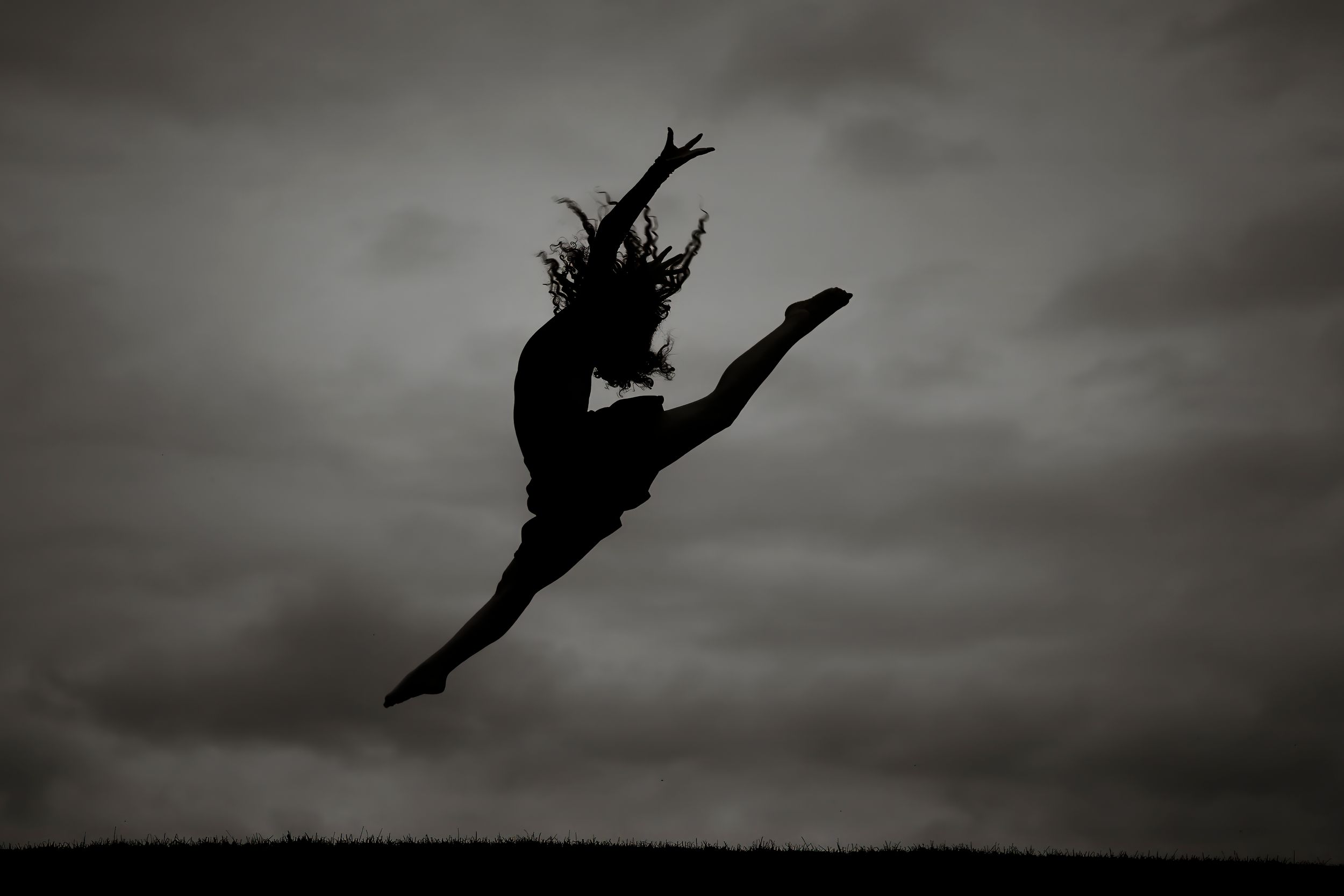 Dramatic silhouettes of dancers leaping and posing against a moody dark sky in a black and white photograph.
