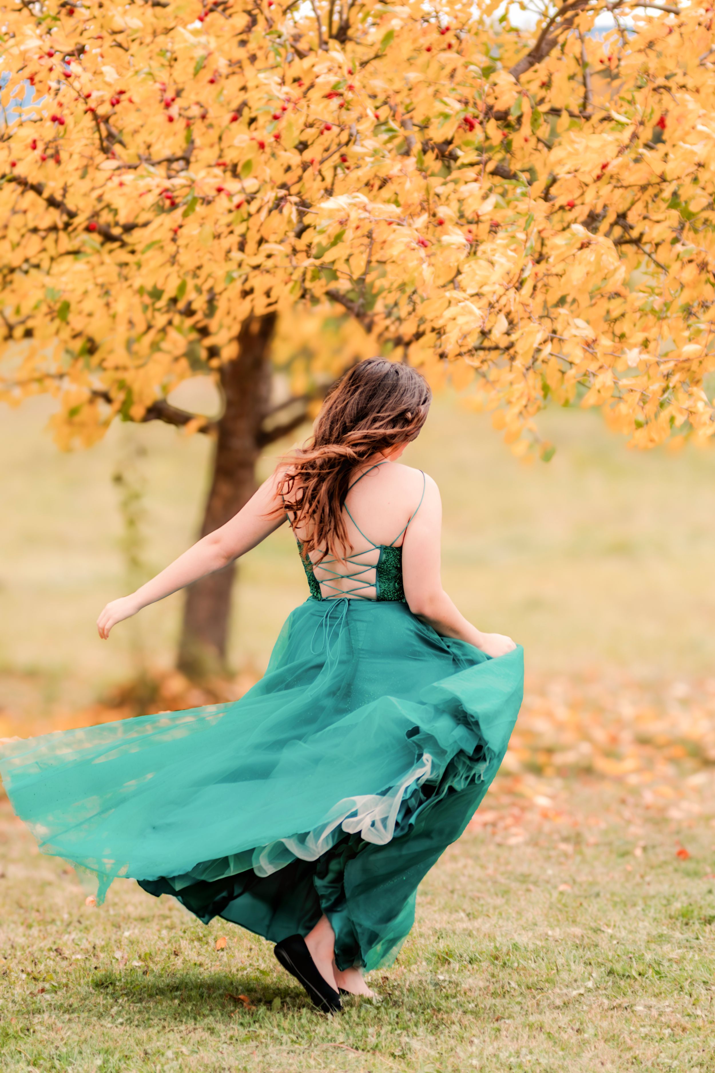 A person in a flowing emerald green dress twirls under autumn trees with golden leaves.